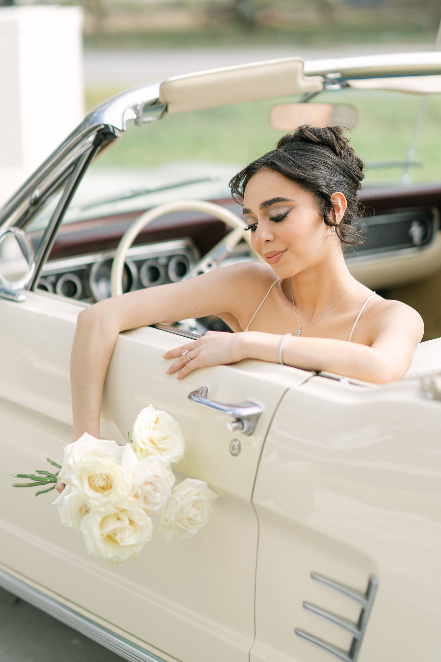 Bride poses elegantly with white roses in classic cream-colored vintage car.