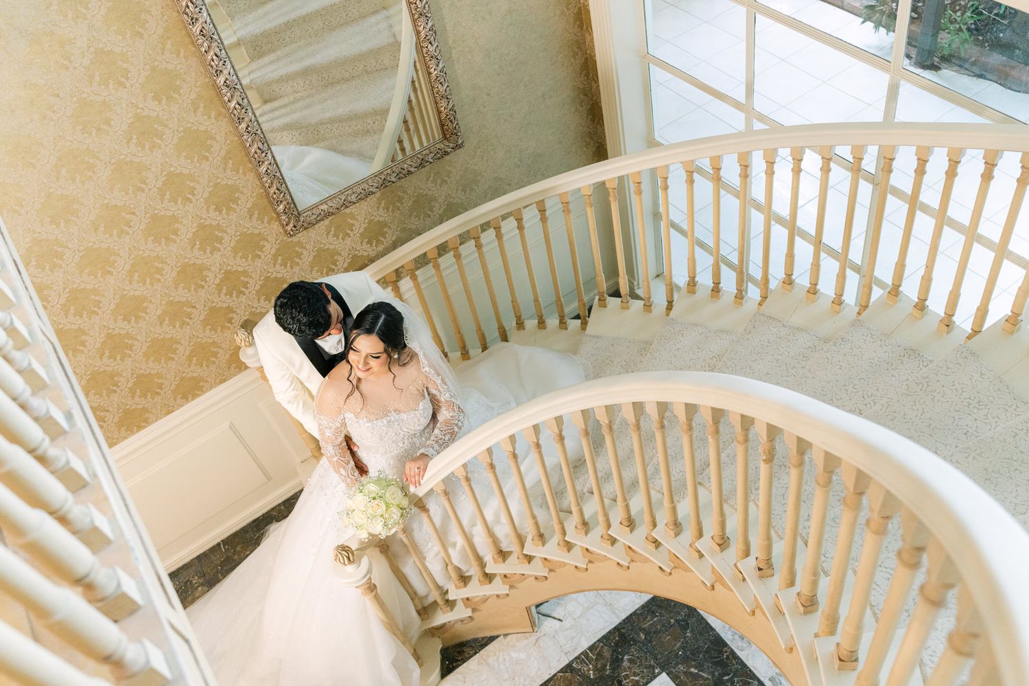 Couple shares intimate moment on elegant curved staircase during wedding photoshoot.