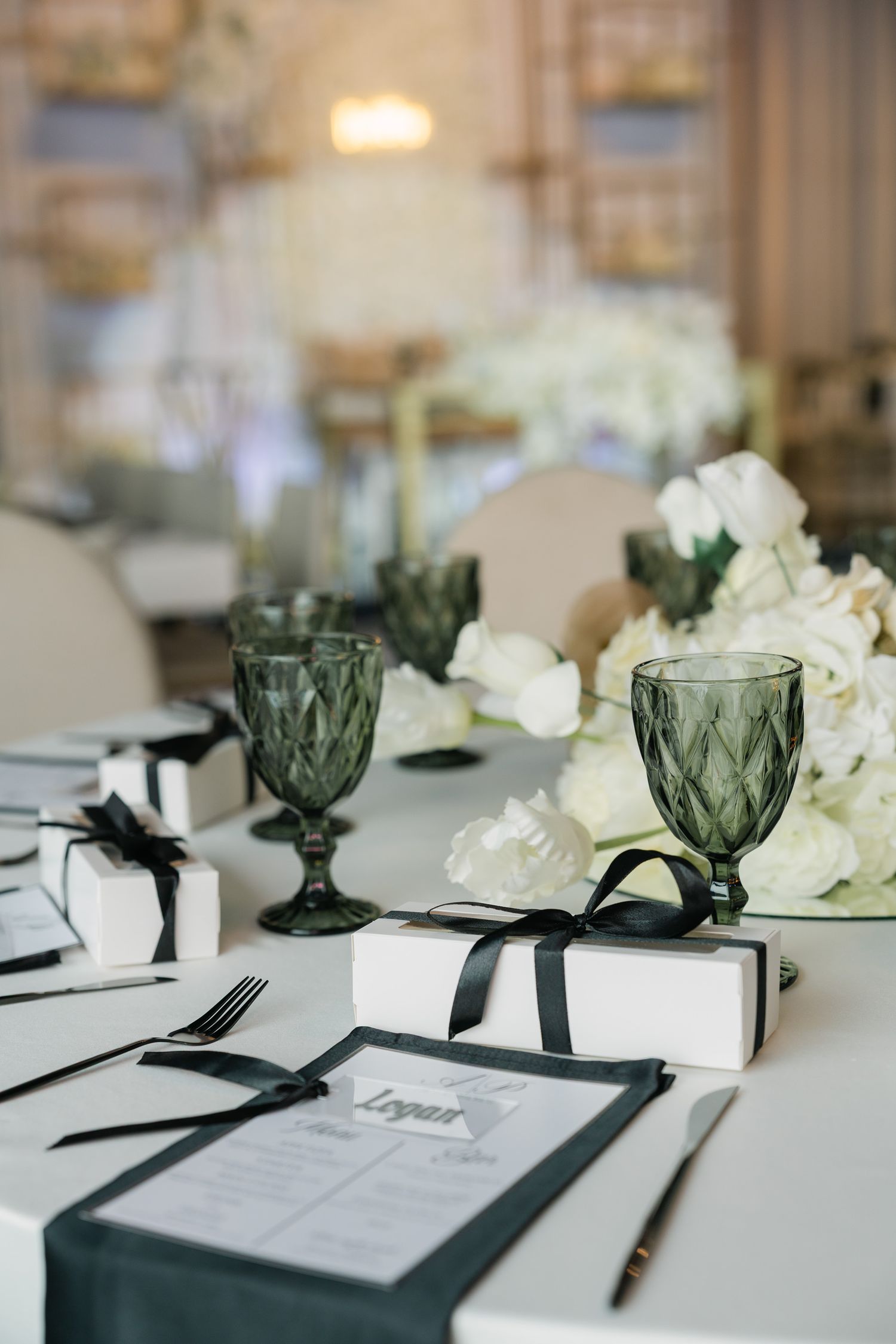 Elegant wedding table setting with green glassware, white gifts, and floral centerpieces.