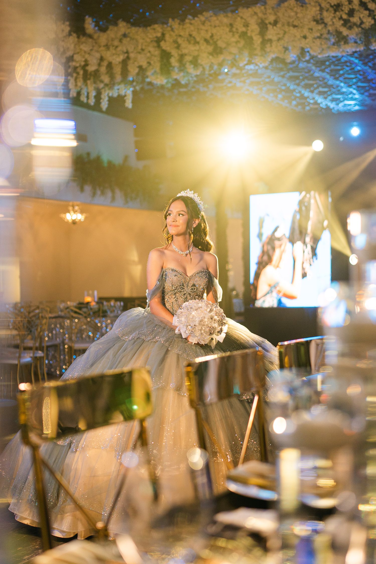 A person in a sparkly ballgown poses during an elegant celebration with dramatic lighting.