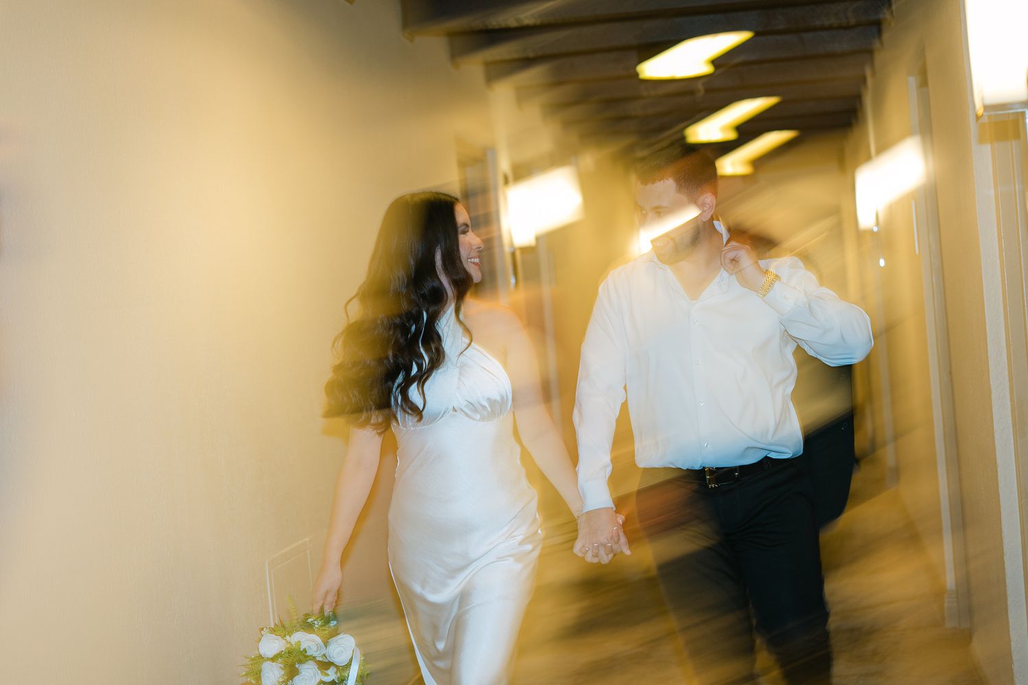 Motion-blurred photo of a couple walking down a hallway in wedding attire.