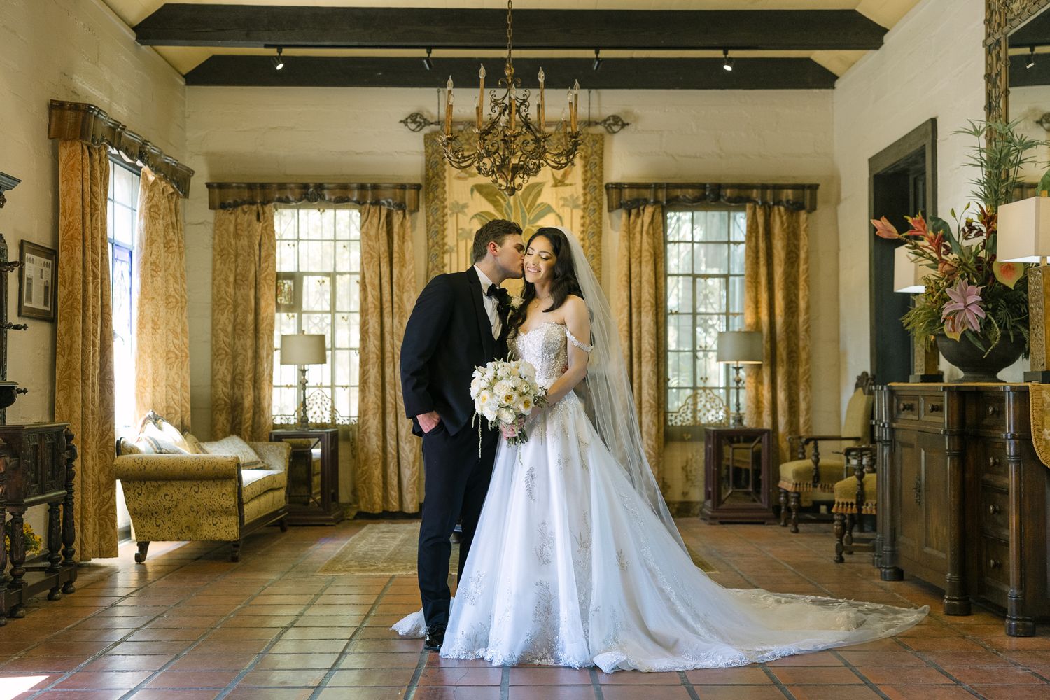 Bride and groom share a romantic kiss in an elegant Spanish-style villa ballroom on their wedding day.
