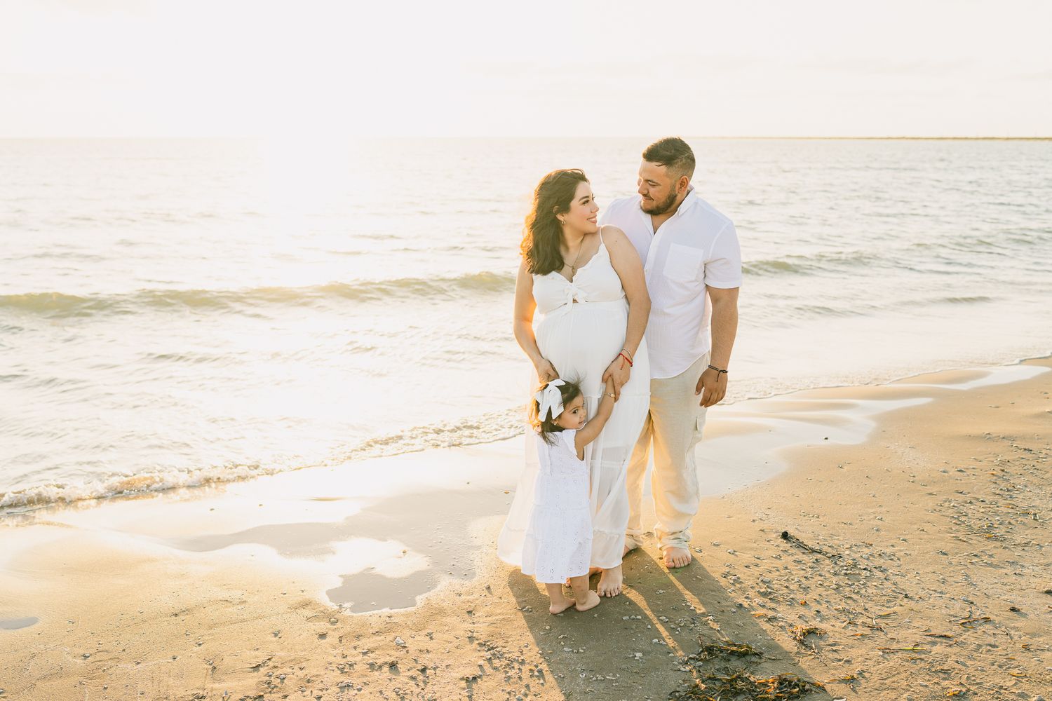 Couple walking hand in hand along peaceful beach during sunset maternity session.