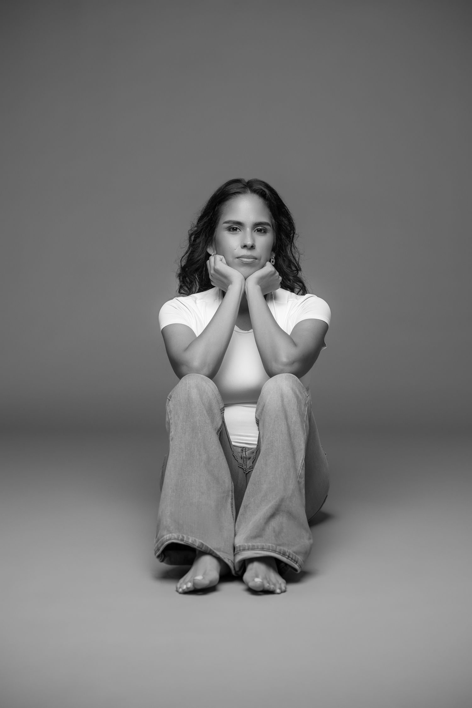 Person sitting with chin resting on hands in contemplative pose against grey backdrop.