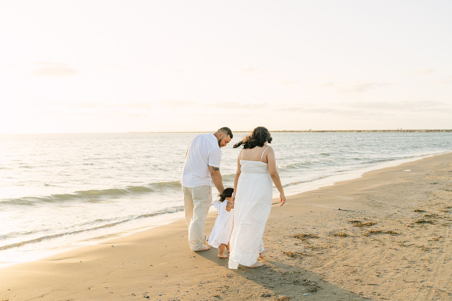 Couple walking together on sandy beach during golden hour maternity session.