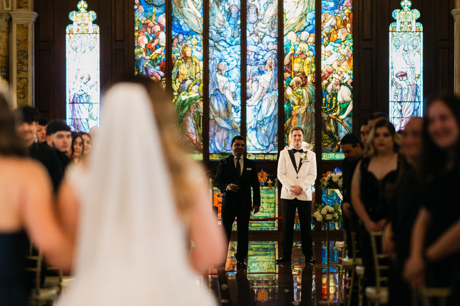 Wedding ceremony in a church with colorful stained glass windows creating a vibrant backdrop.