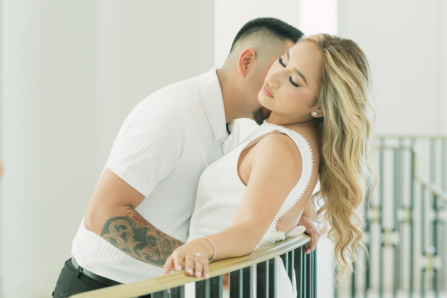 A couple in white clothing embraces on an outdoor balcony railing.
