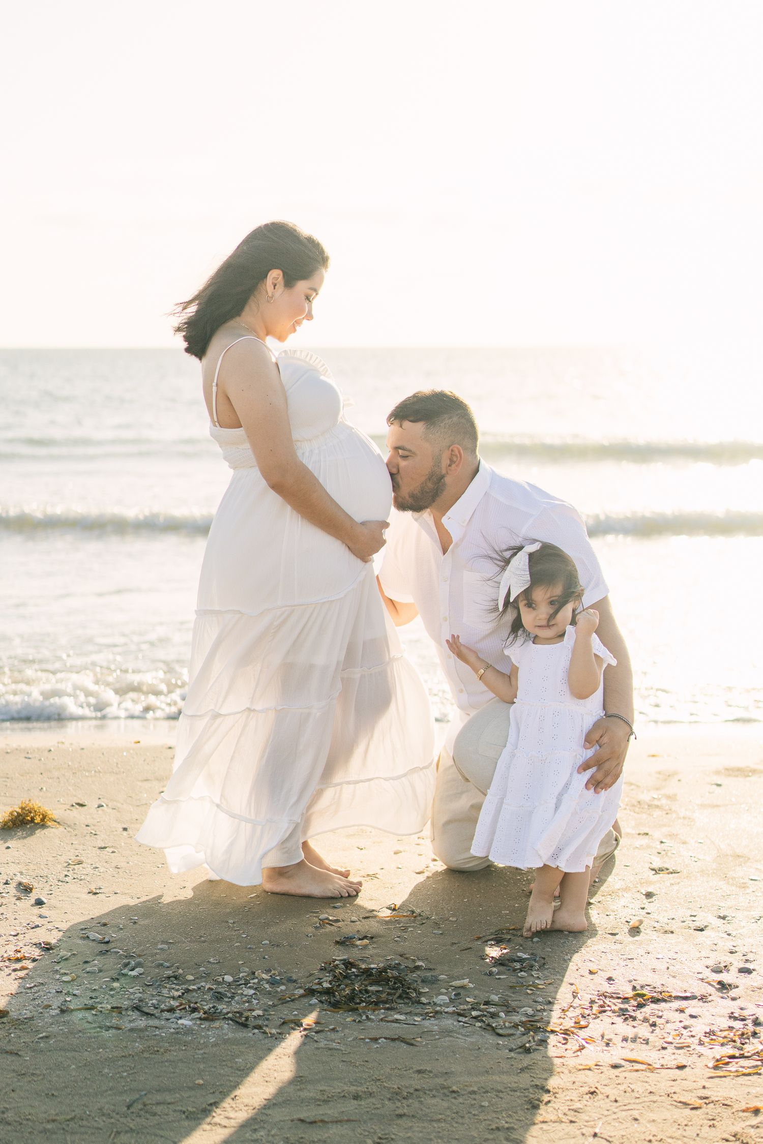Family sharing tender moment on beach at sunset during maternity photoshoot.