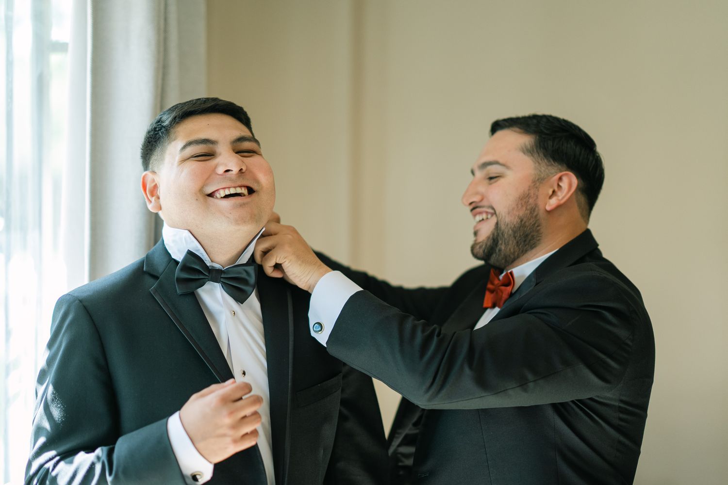 Two groomsmen share a joyful moment while adjusting bow tie before the ceremony.