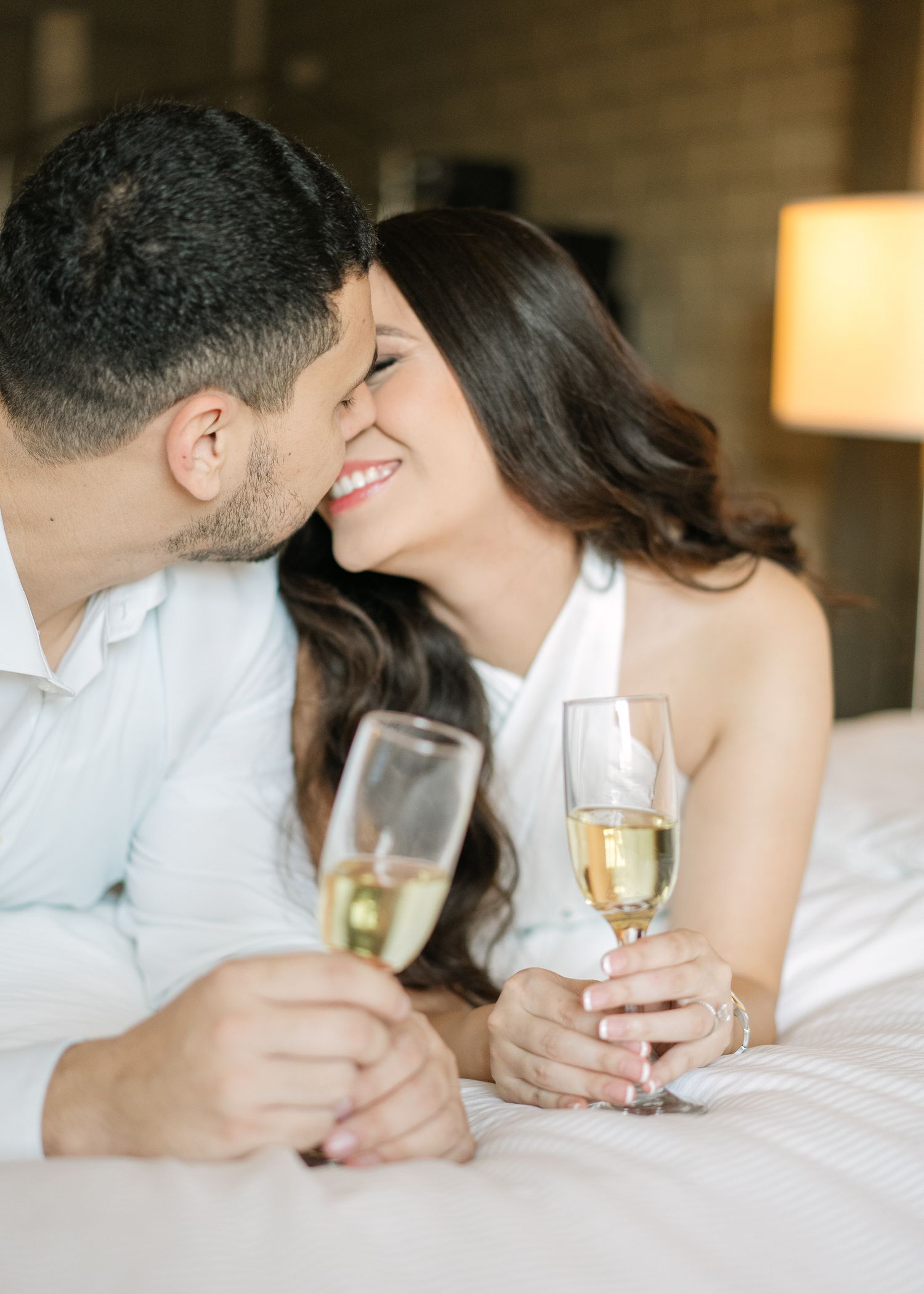 A romantic moment shared with champagne glasses on white bedding.