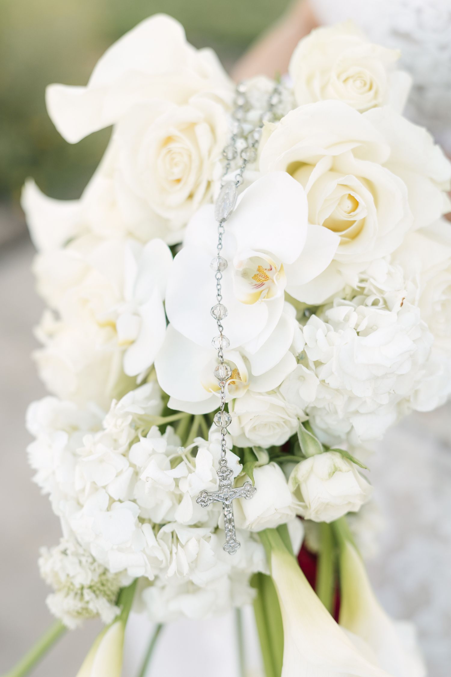 Elegant bridal bouquet of white roses, orchids, and hydrangeas adorned with a silver cross rosary.