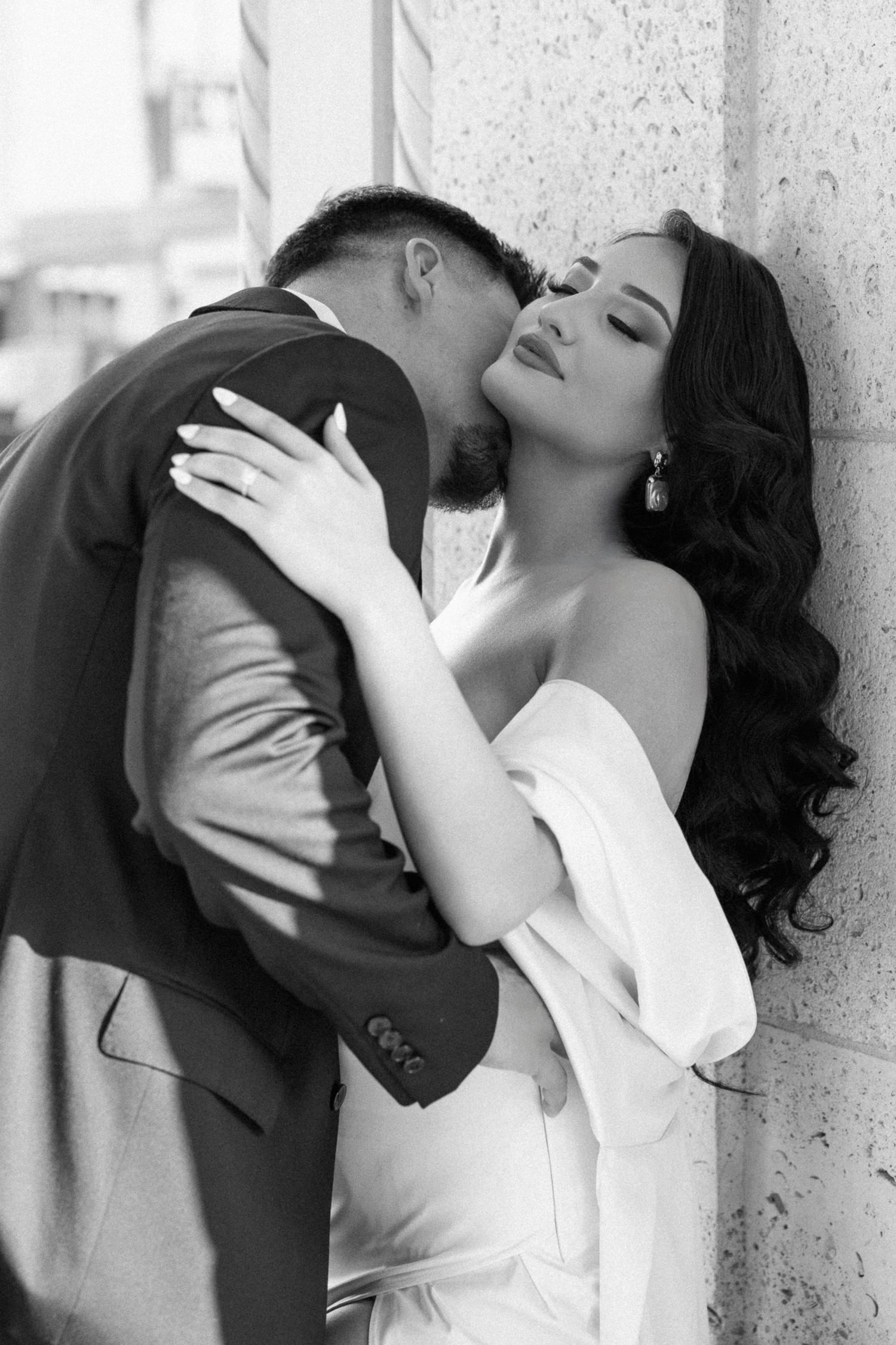 A romantic black and white portrait of a couple sharing an intimate moment against a wall.