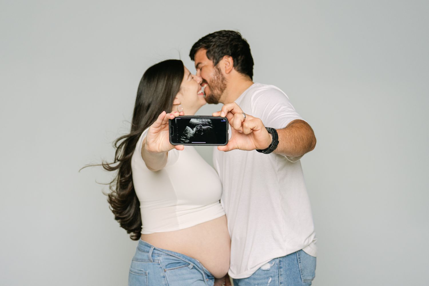 Casual maternity photography session showing couple in light clothing sharing intimate moments.