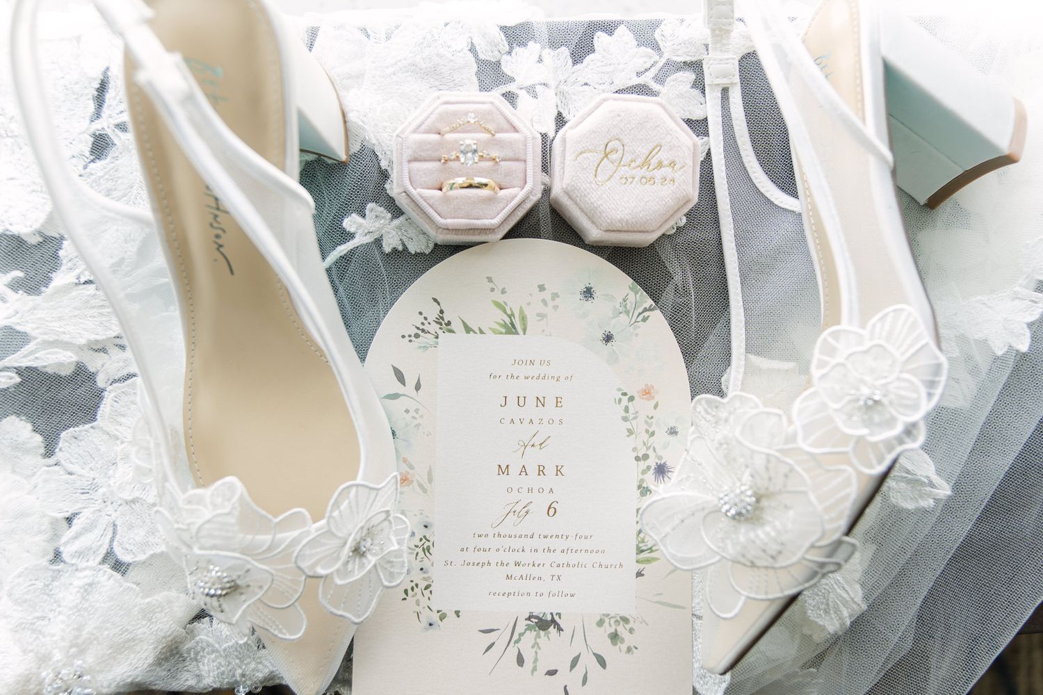 Delicate white wedding stationery and floral arrangements displayed on a soft gray surface.