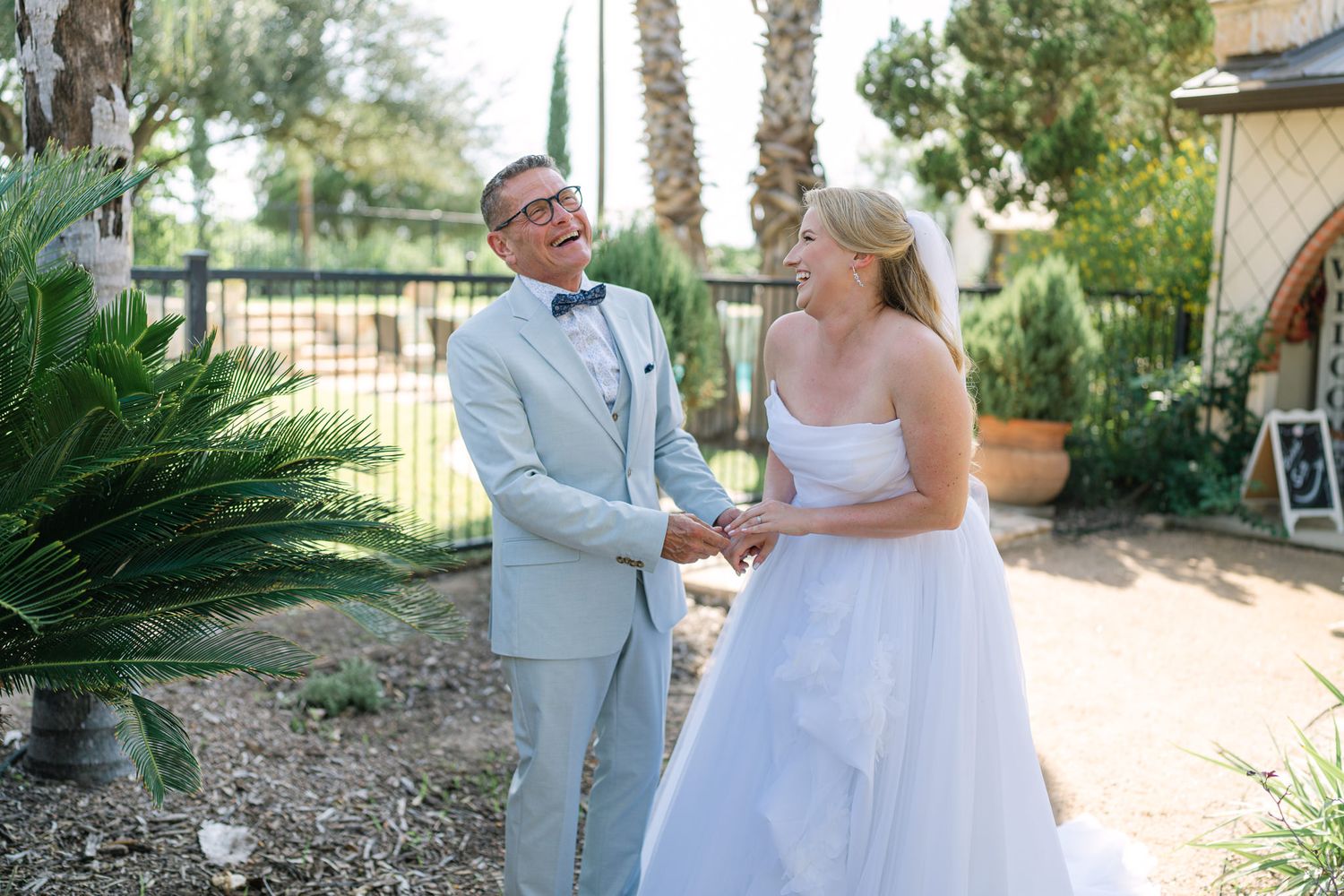 Joyful wedding couple sharing a laugh during outdoor ceremony near palm trees.