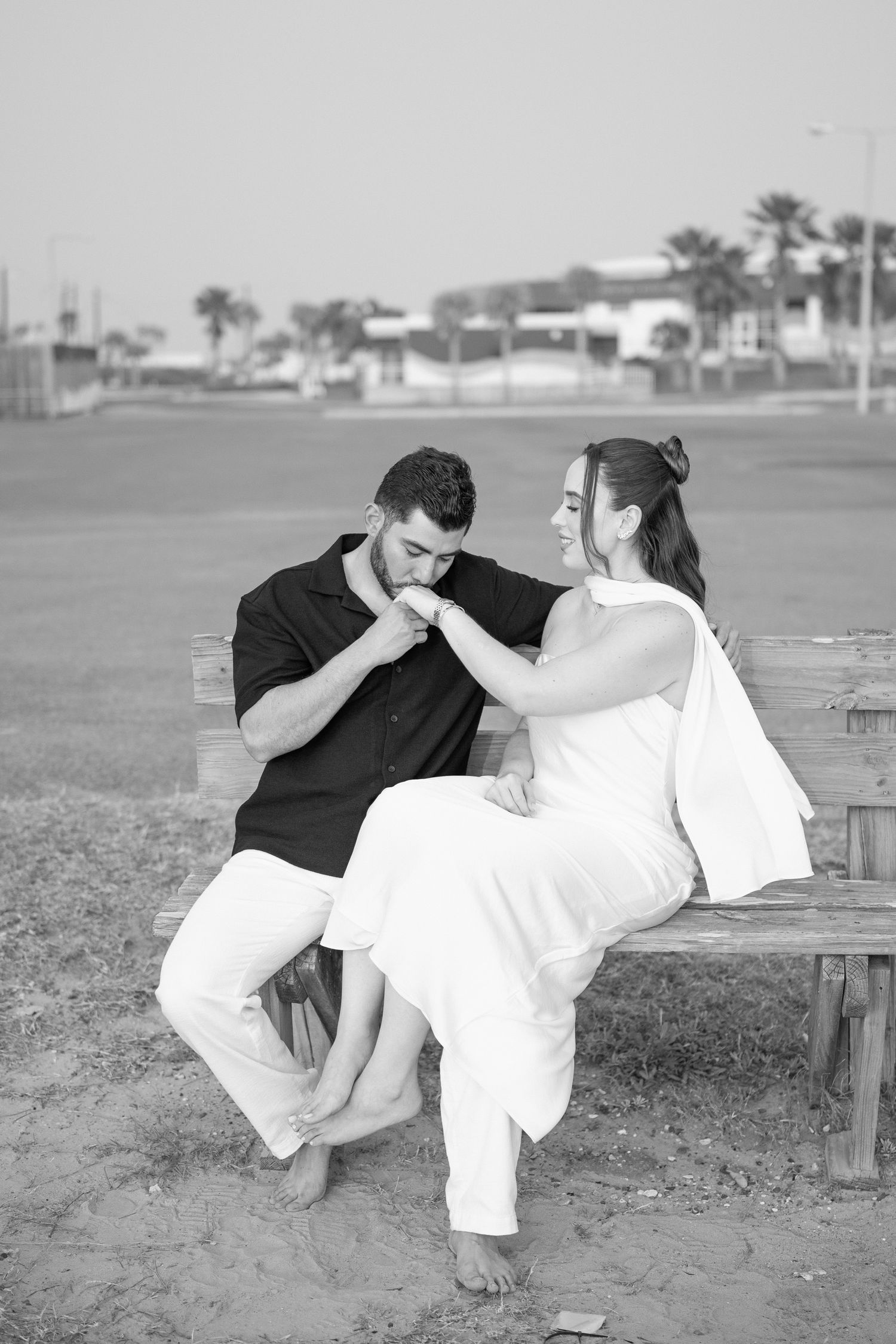 A couple shares a tender moment on a wooden bench at the beach.