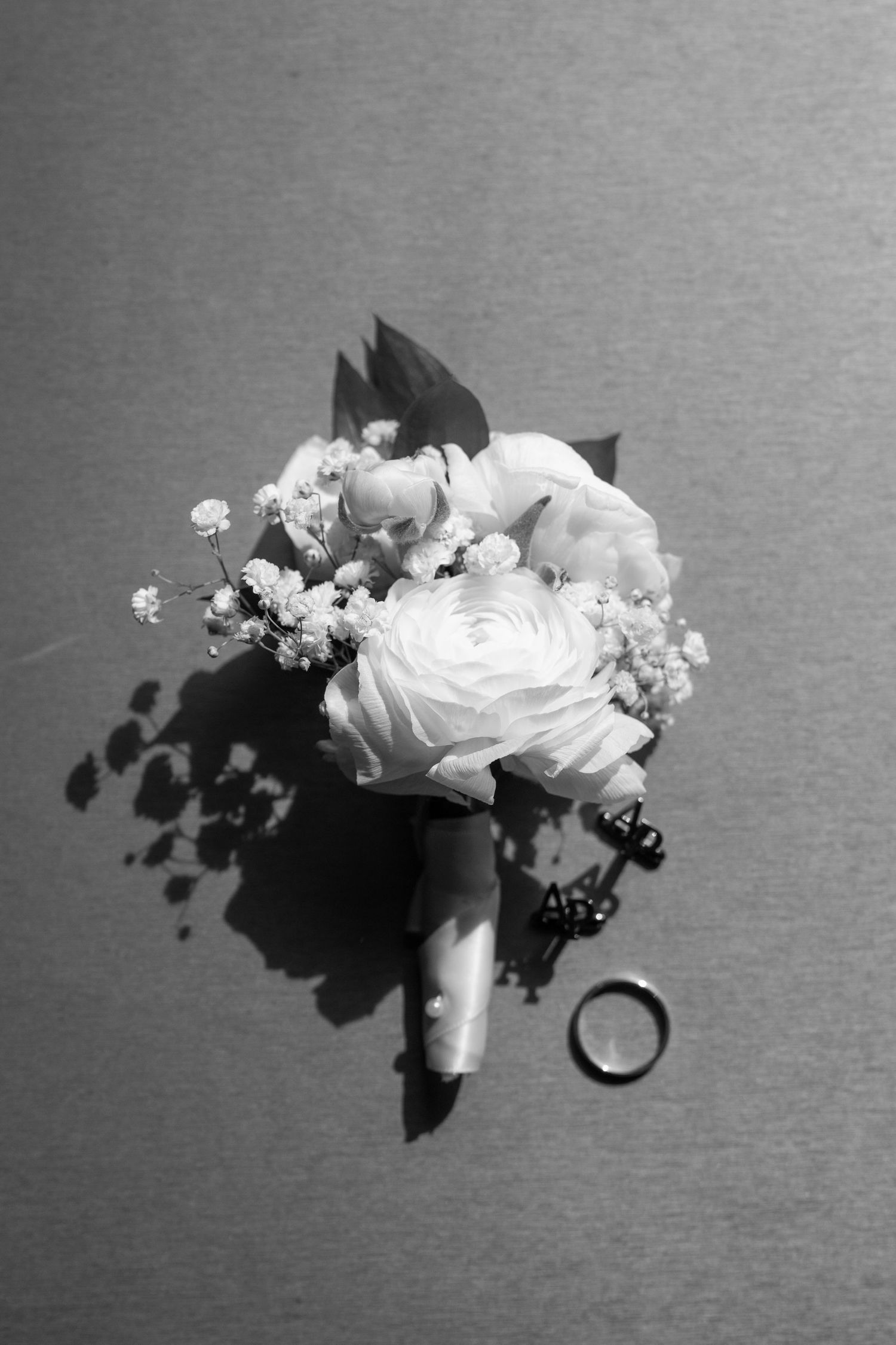 Black and white wedding photo of a rose bouquet with a wedding ring casting a shadow on a plain surface.