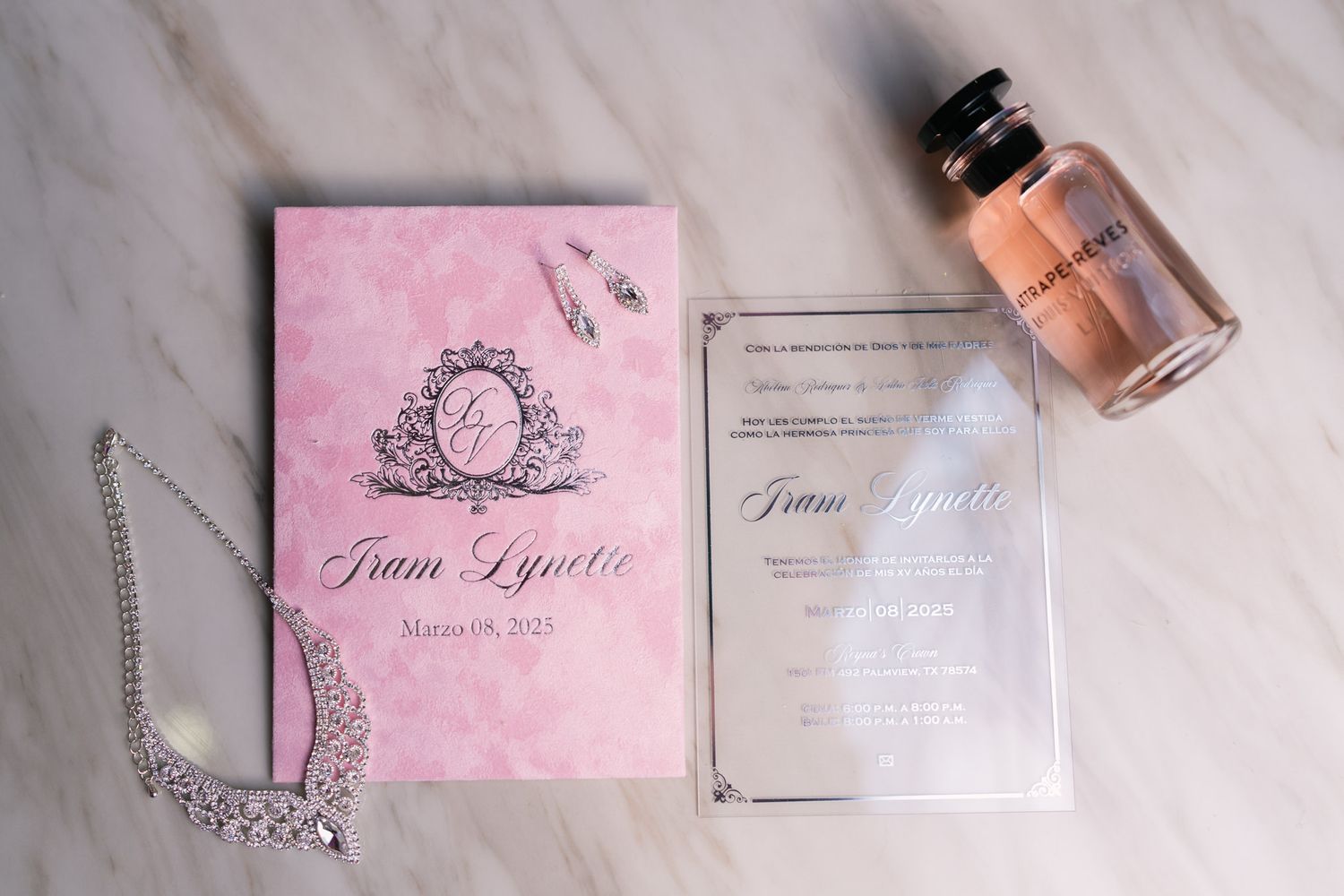 Wedding stationery layout with pink invitations, perfume bottle, and decorative elements on marble surface.