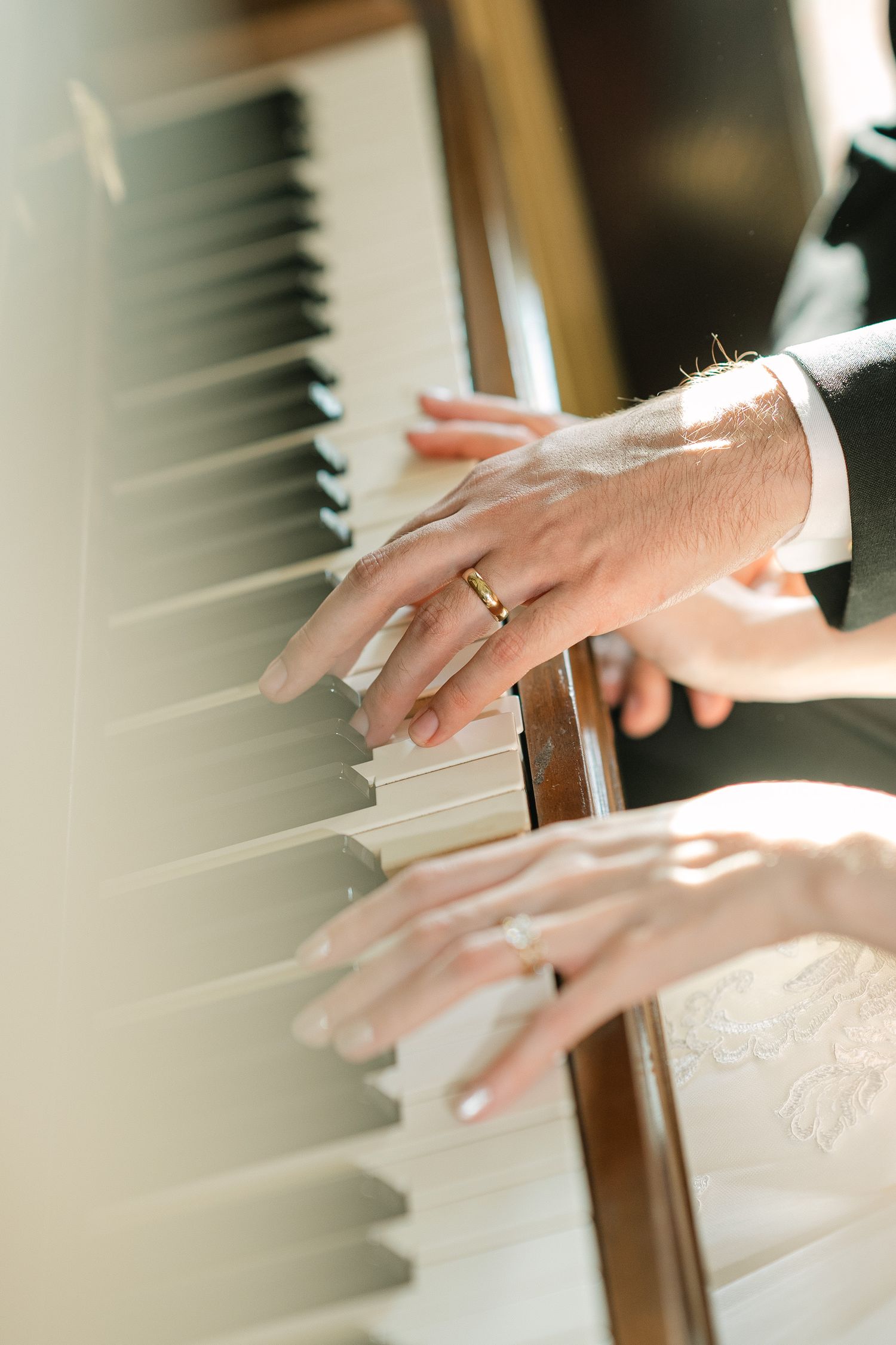 Hands playing piano keys in soft natural light, showing wedding ring detail.