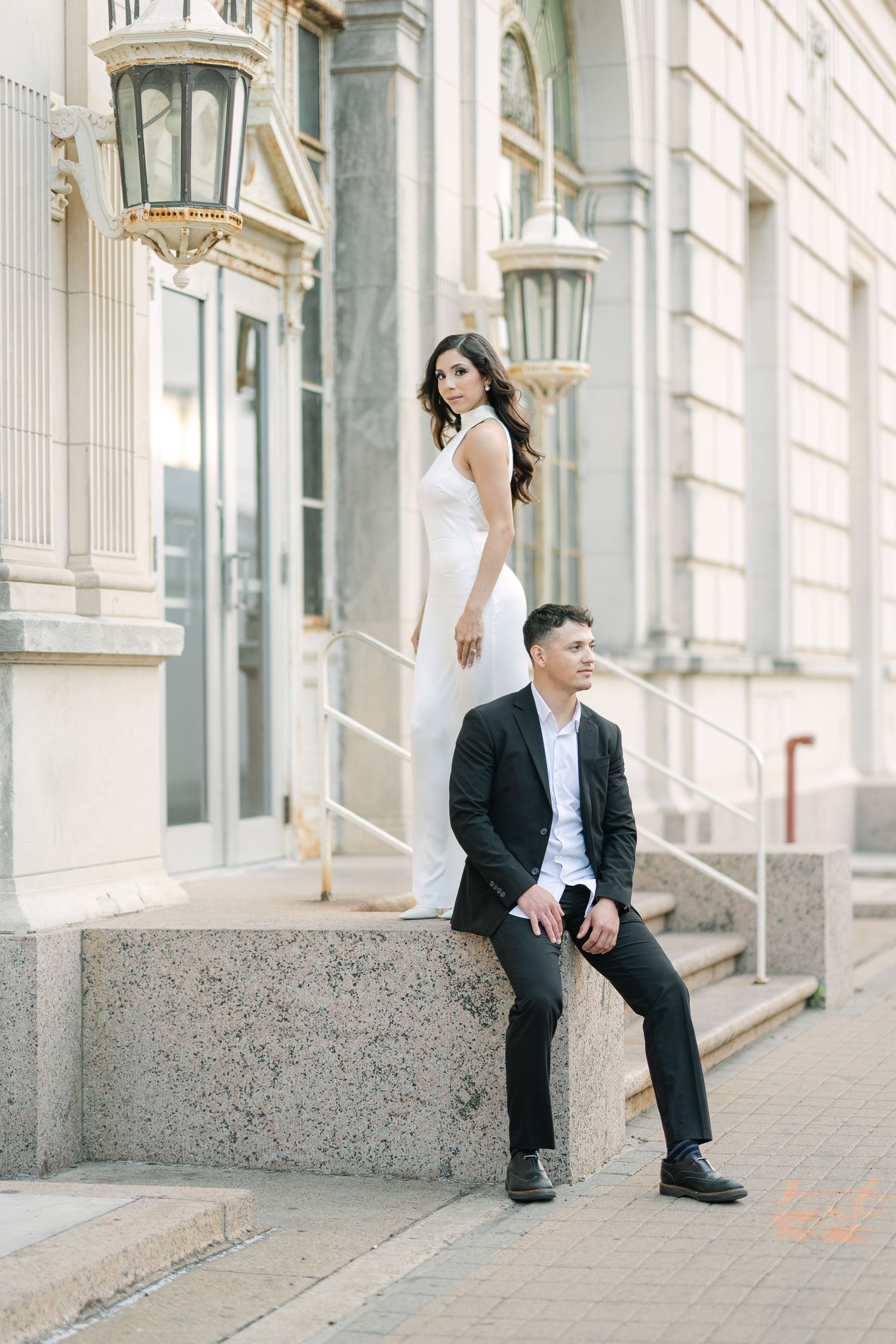 An elegant couple poses on stone steps with vintage lanterns and classic architecture.