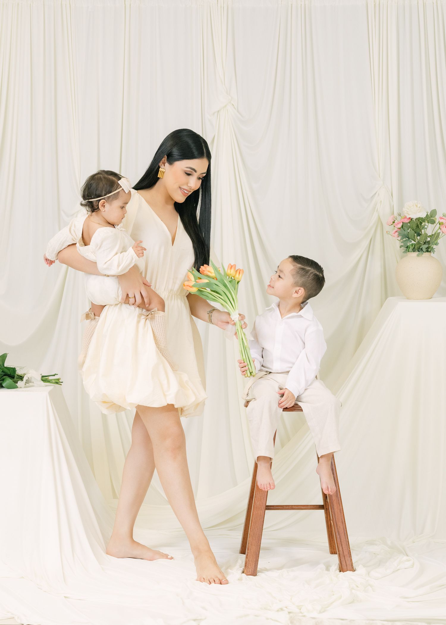 Sweet family moment with mother and children holding flowers against white backdrop.