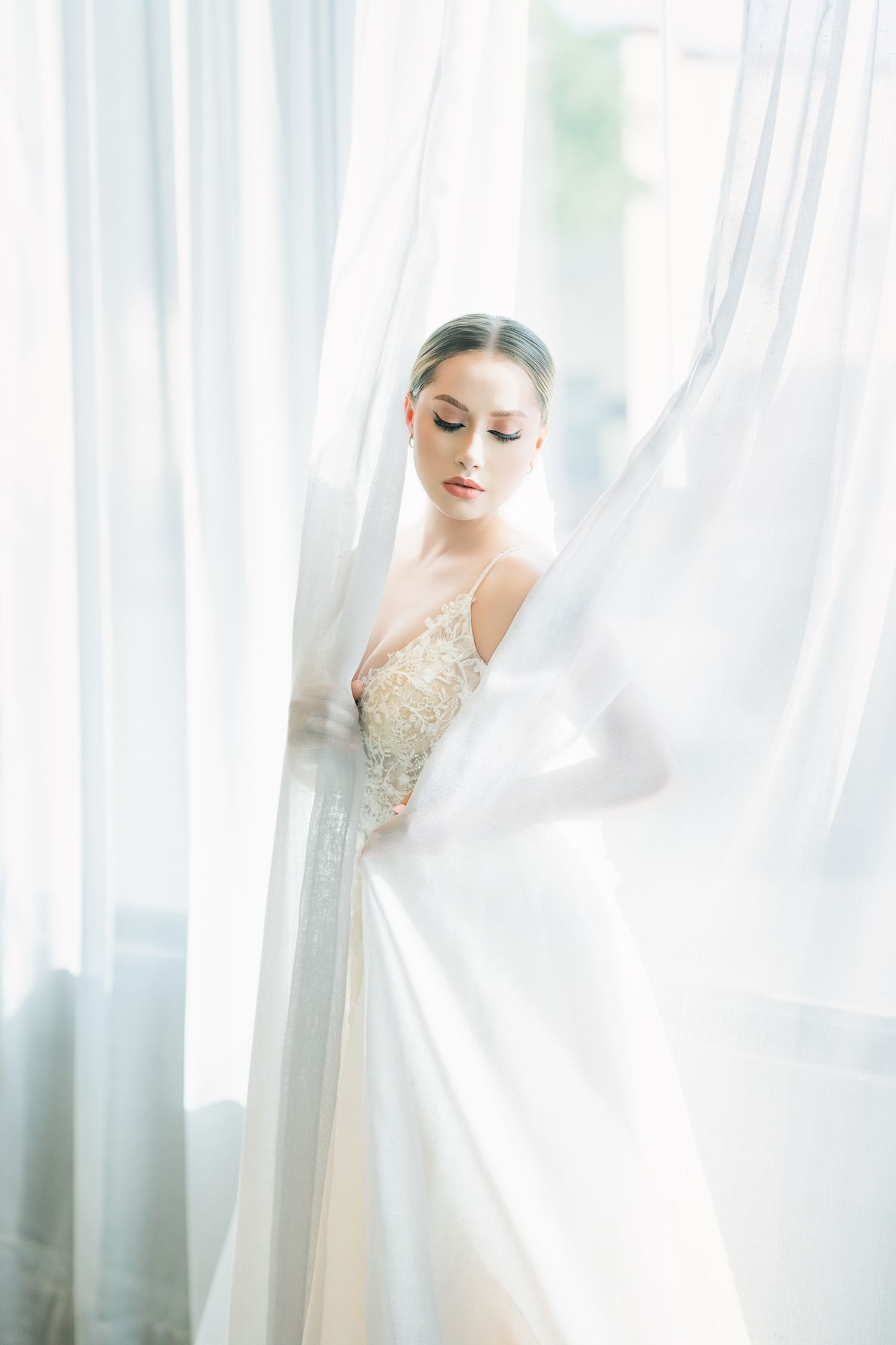 Dreamy bridal portrait with sheer curtains creating a soft, romantic atmosphere.