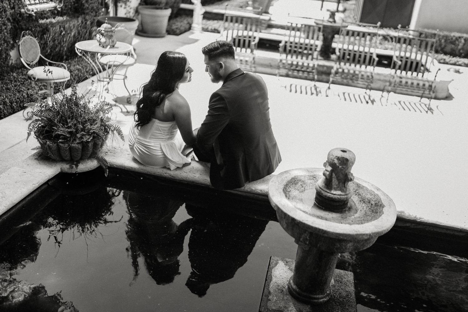 A black and white photo of a couple seated on a bench in a garden setting with decorative elements.