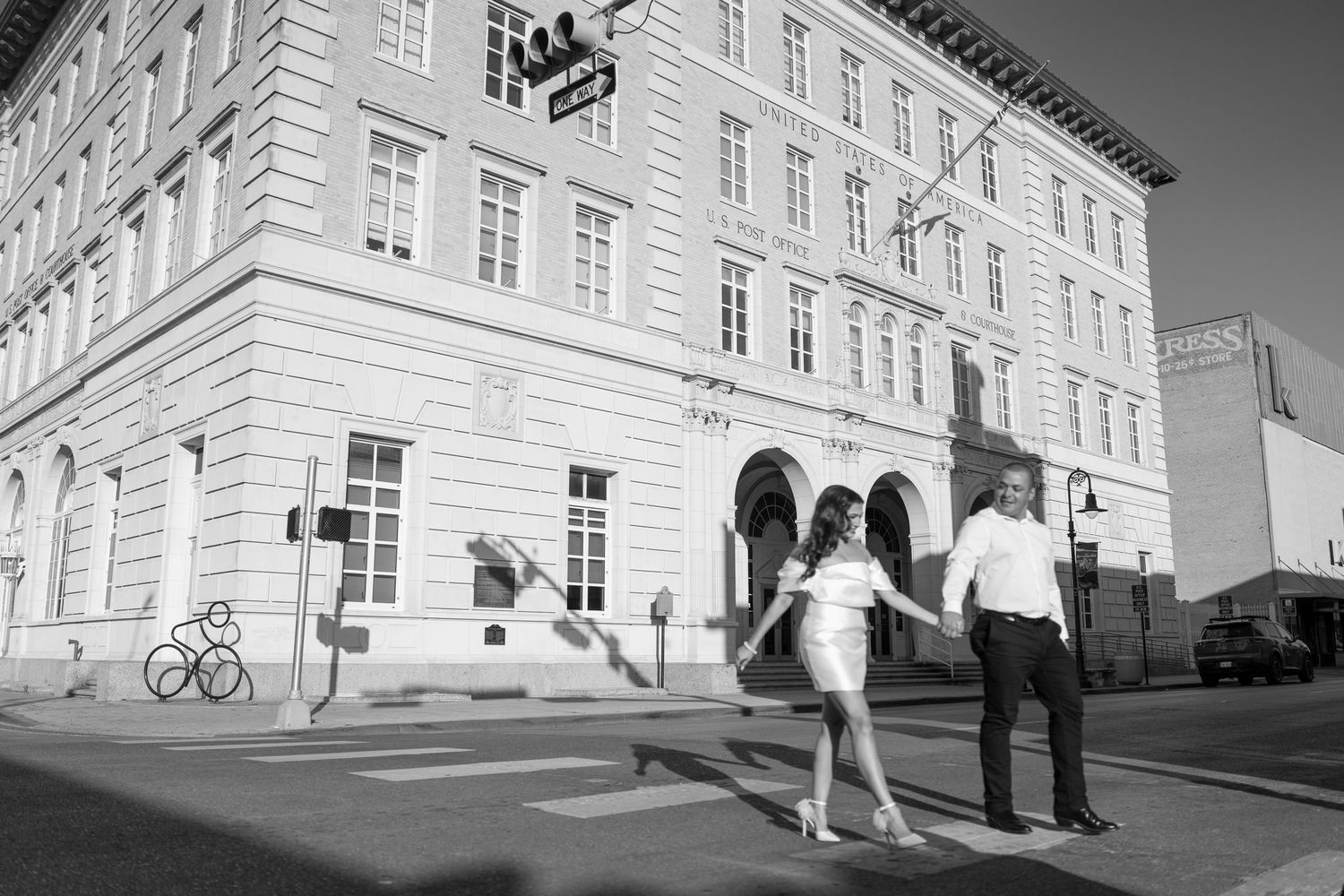 A couple walks together near a historic building in black and white photography.