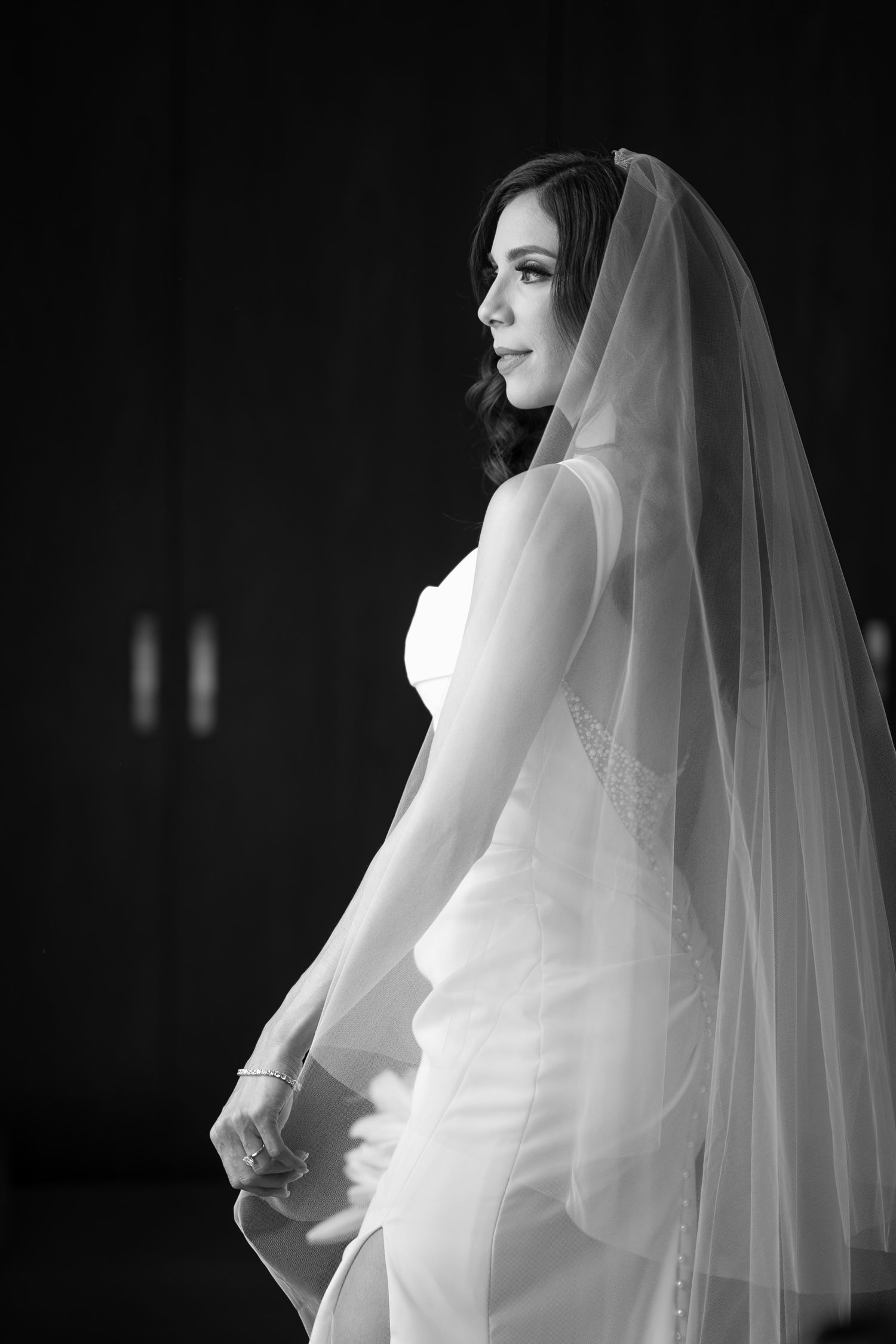 Elegant side profile of bride in white gown and flowing veil.