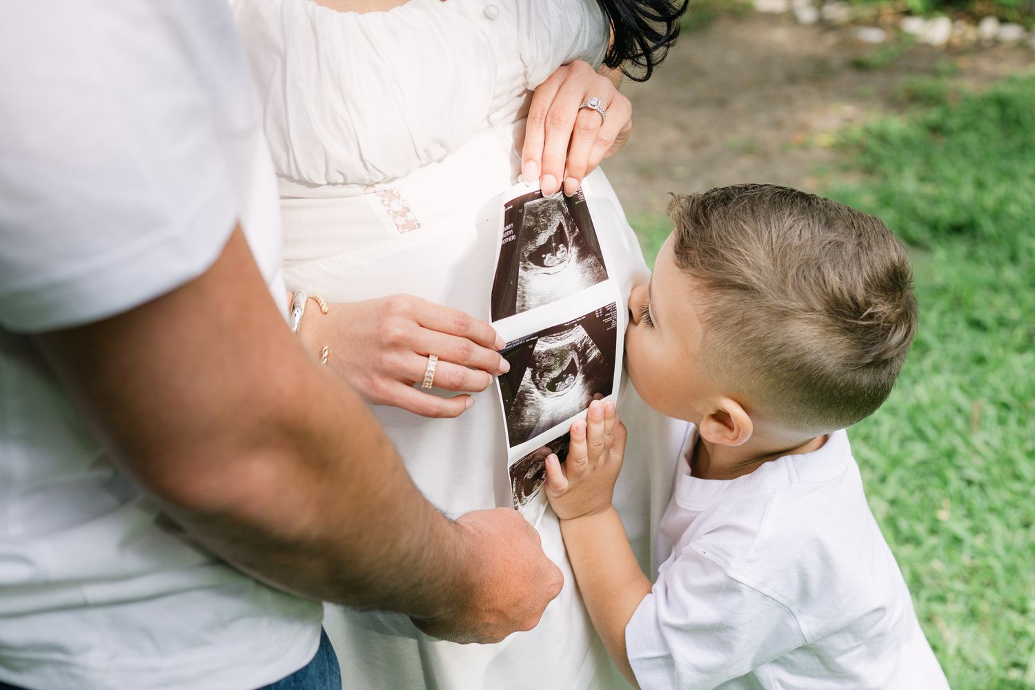 Child looking at ultrasound photo while touching pregnant belly.