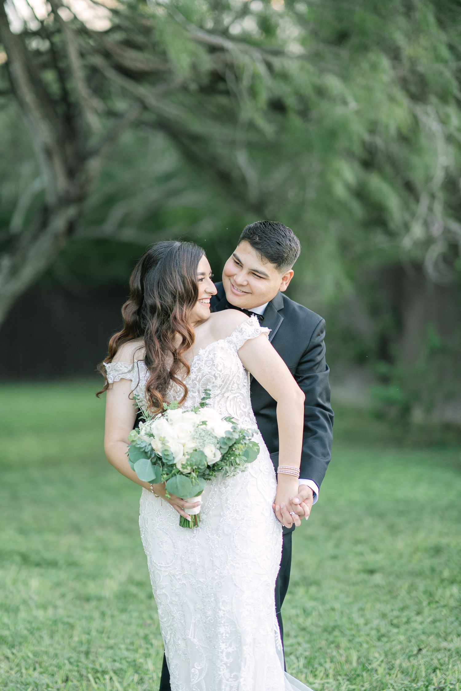 Romantic garden portraits of wedding couple amongst greenery with white floral bouquet.