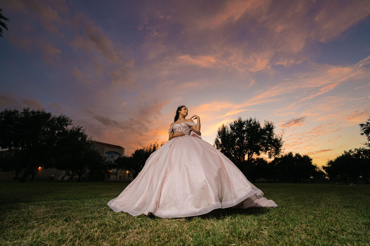 Bride in white gown lies on grass during dramatic sunset photoshoot.