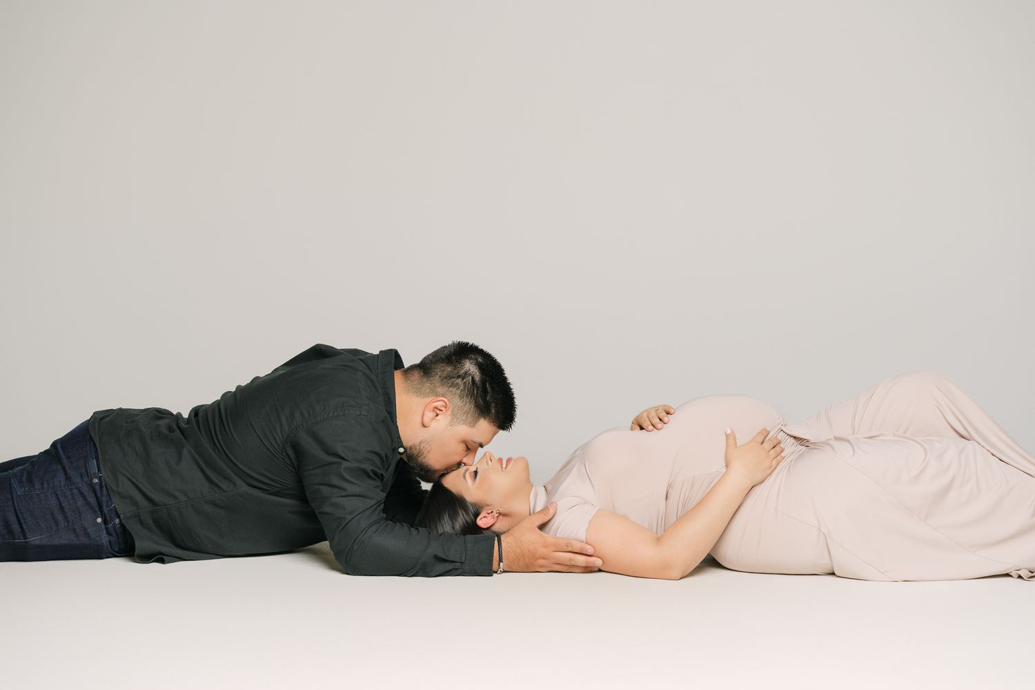 Creative maternity photo series showing couple lying down in neutral studio setting.