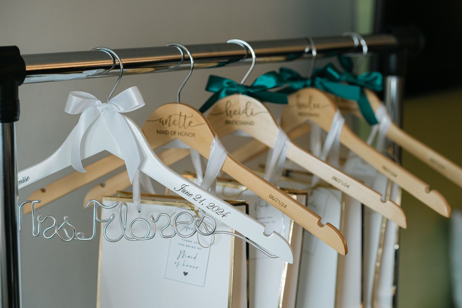 White wooden hangers with personalized names displayed on a clothing rack for a wedding.