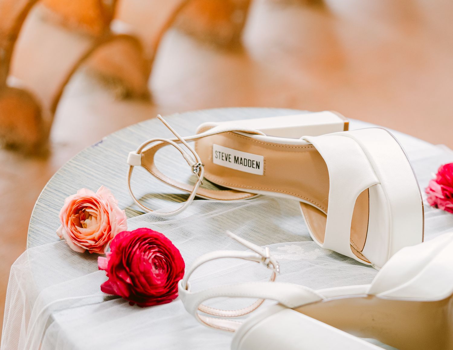 Elegant wedding details including rings, invitations, and red roses arranged on a light beige surface.