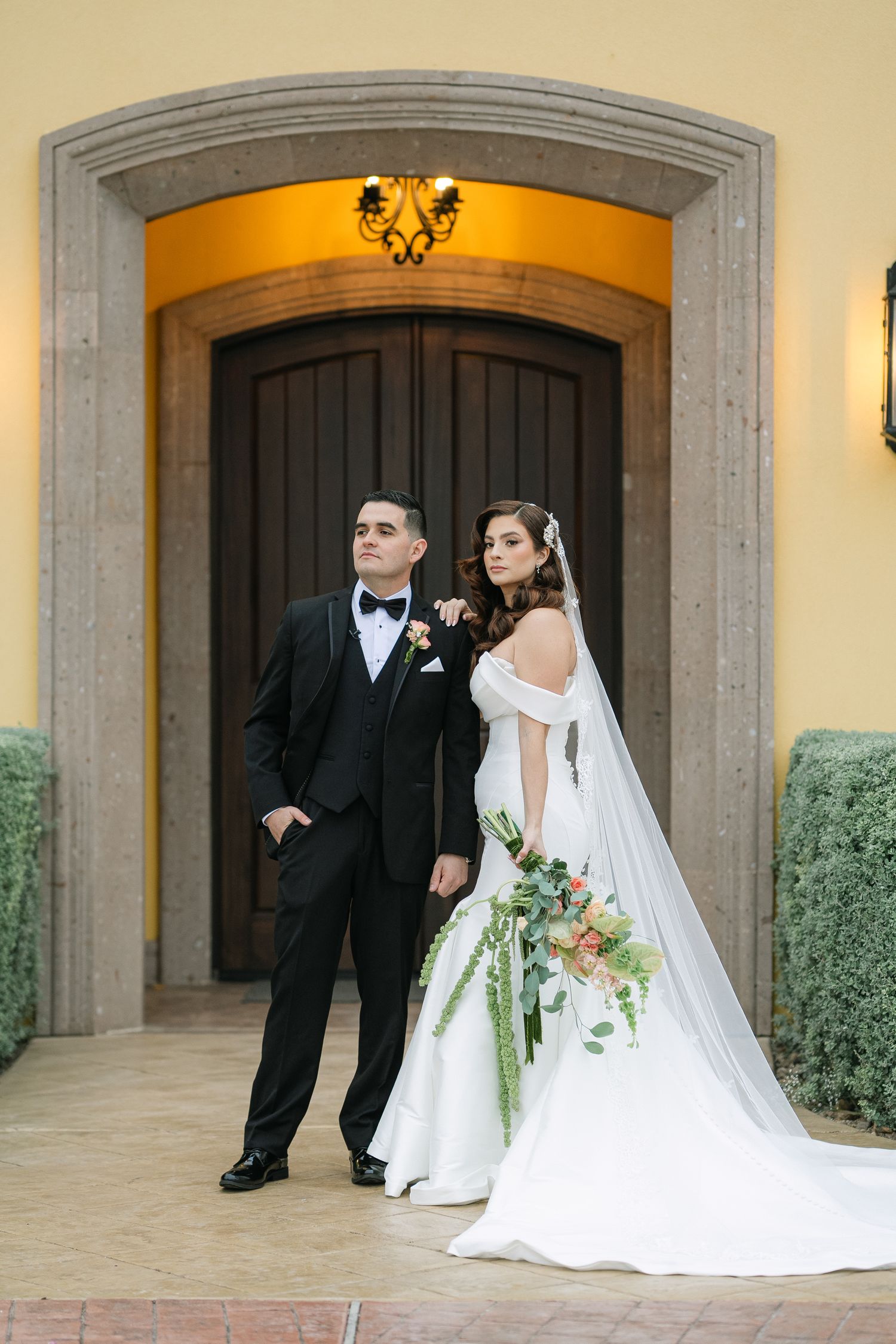 Bride and groom pose elegantly in front of yellow Spanish-style archway.