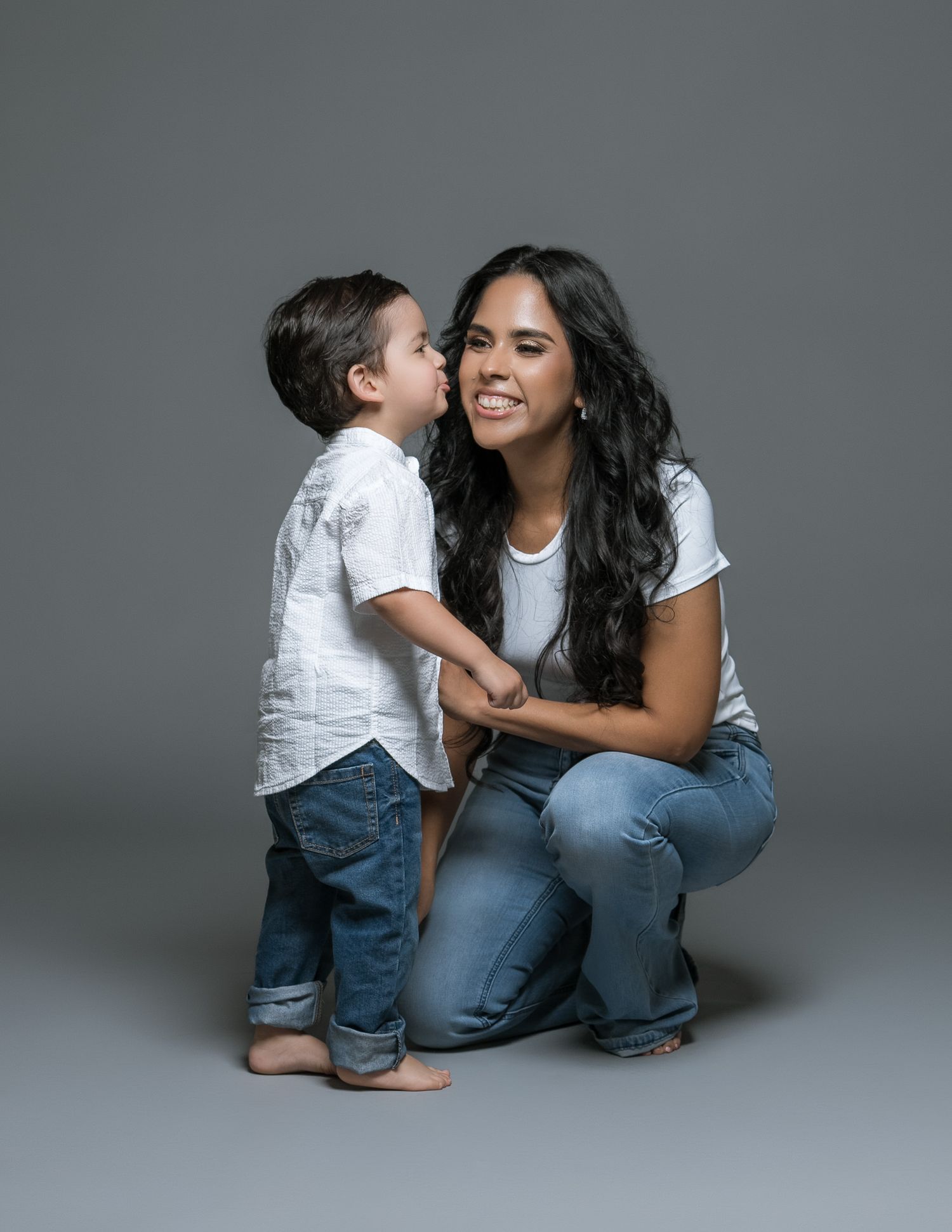 Heartwarming studio portrait of parent and child sharing a joyful moment against grey background.