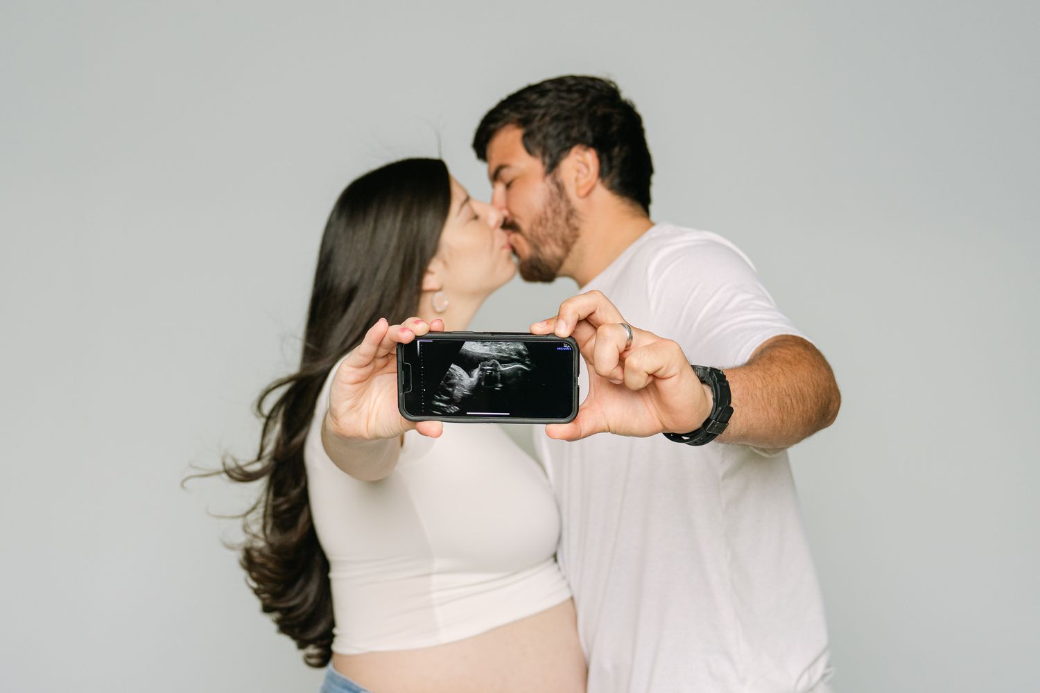 Couple holding ultrasound photo while kissing in studio setting.
