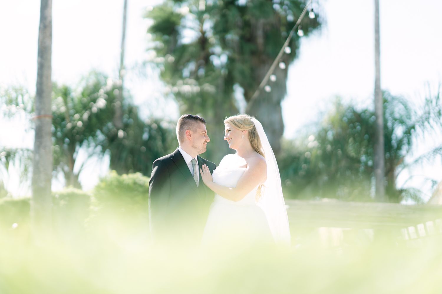 A romantic outdoor wedding portrait with soft sunlight filtering through trees.