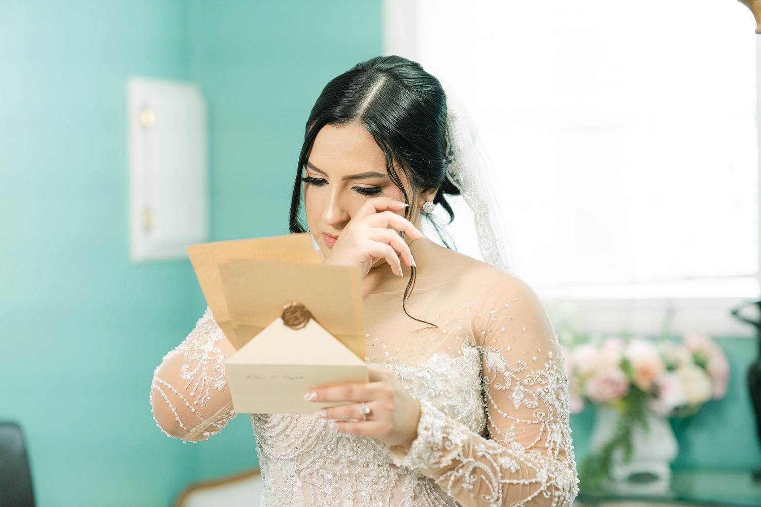 Emotional bride in lace dress reads letter during wedding day preparations.