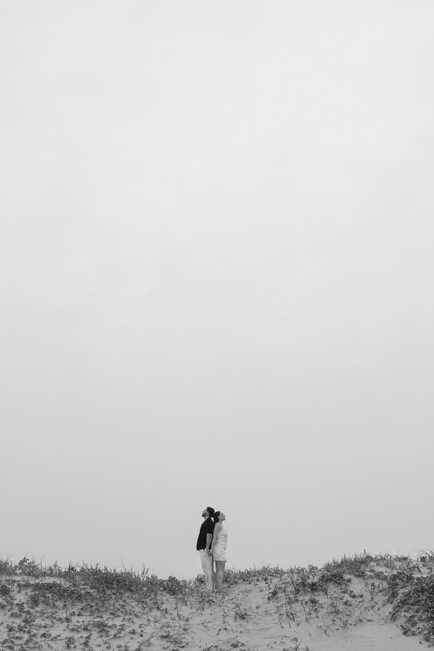 A minimalist black and white photo of two people embracing on a sandy hill.
