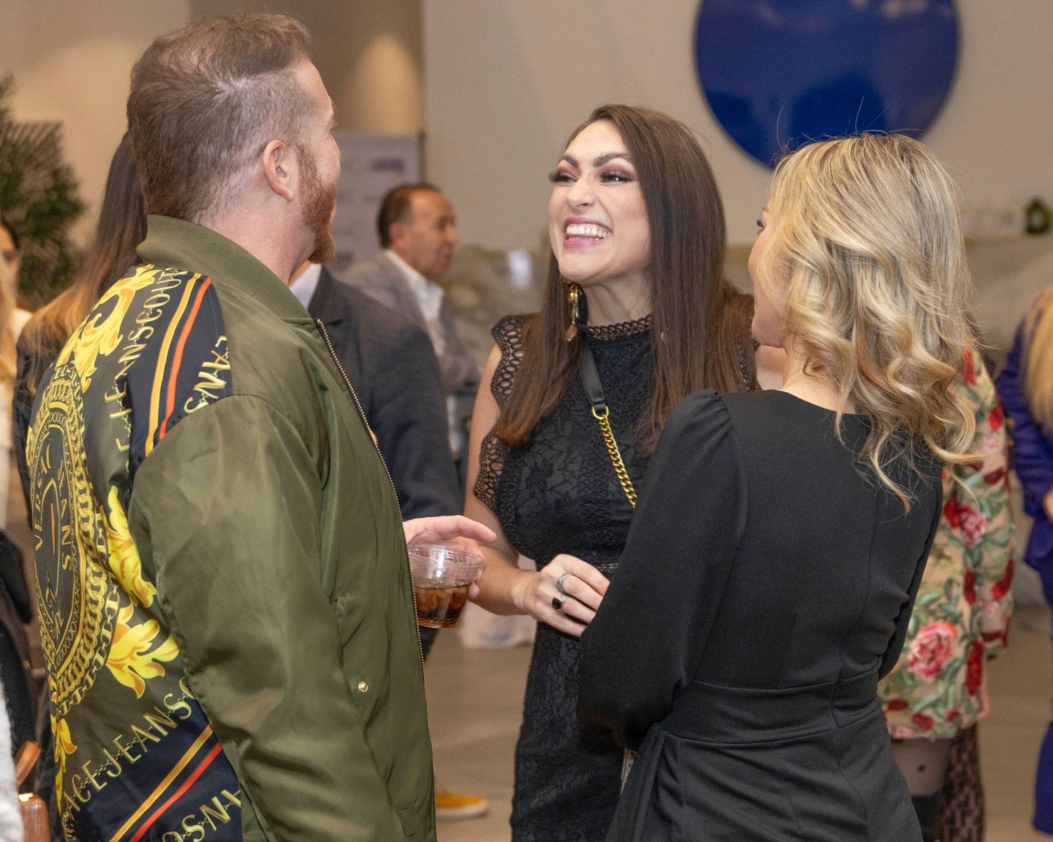 Guests socializing at an evening reception with blue decor elements visible in the background.