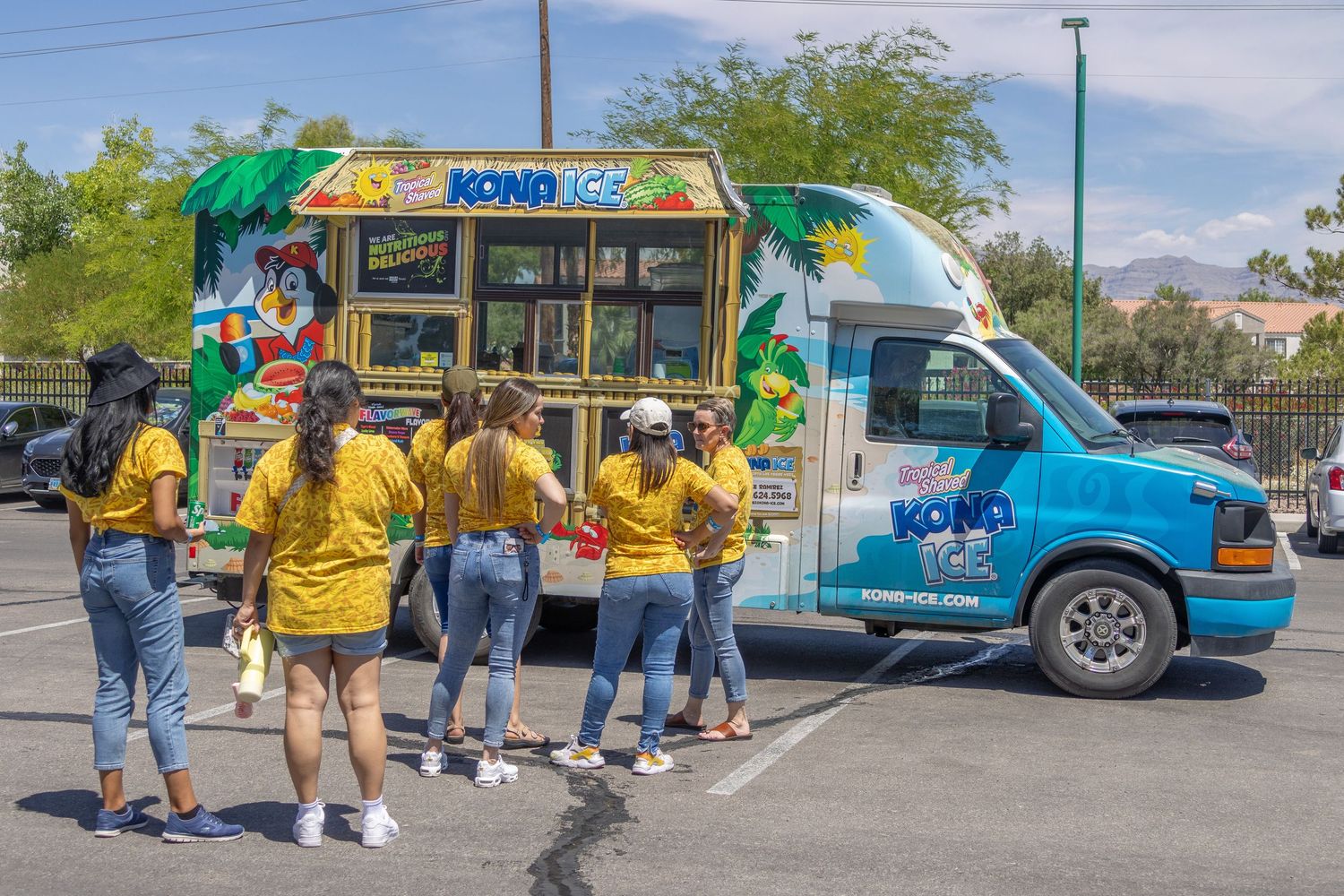 A row of snack food trucks and customers line up at an outdoor venue during a sunny day.