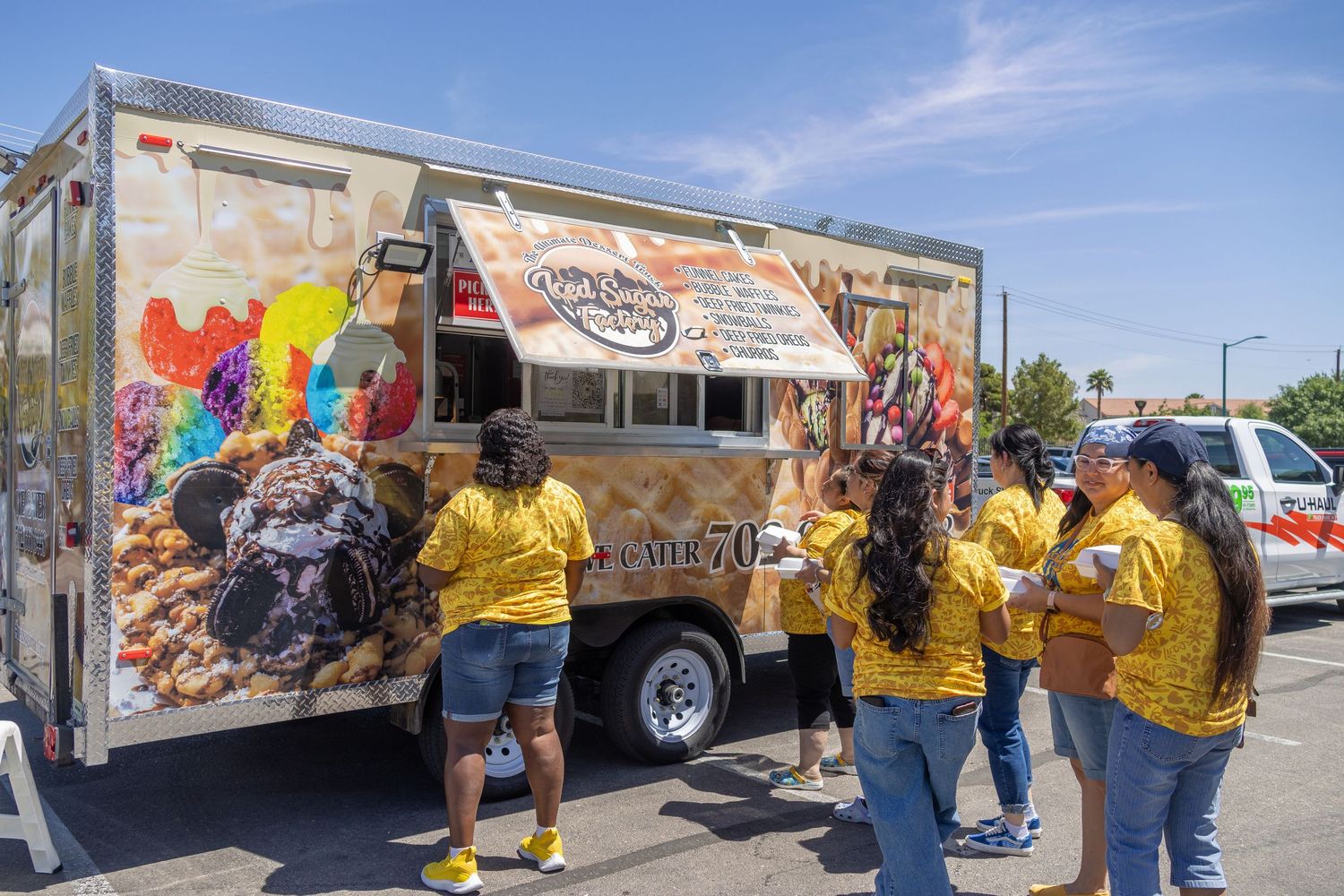A row of colorfully graffitied delivery trucks parked along a city street with people gathered around them.