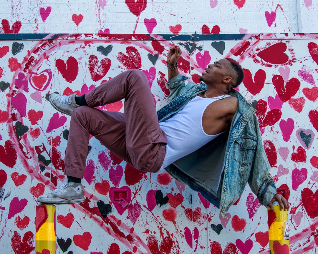Someone performs a backflip against a wall decorated with red and pink heart patterns.
