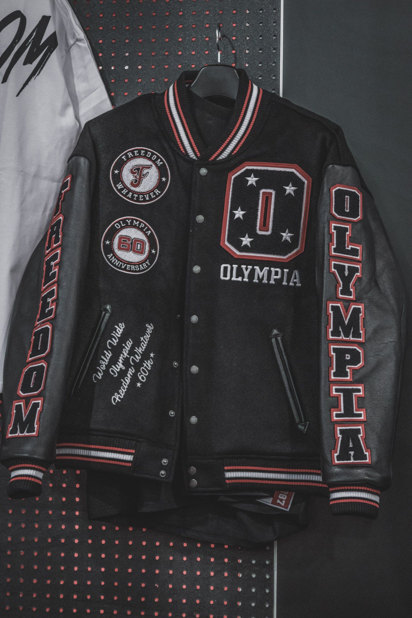 Black varsity letterman jacket with red and white trim featuring Olympia patches and embroidered details on dark background.