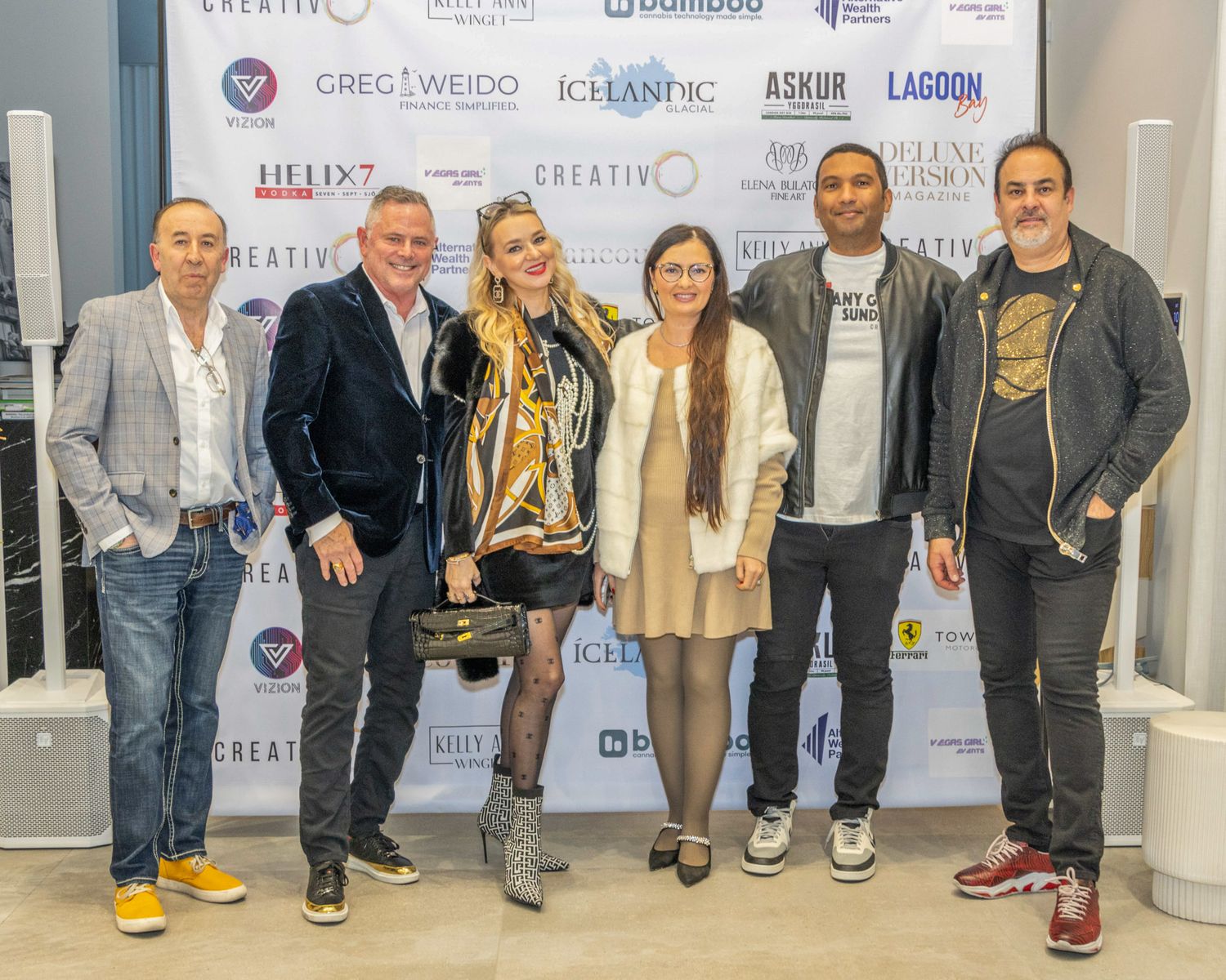 Corporate event photo showing group of people posing in front of branded sponsor wall.