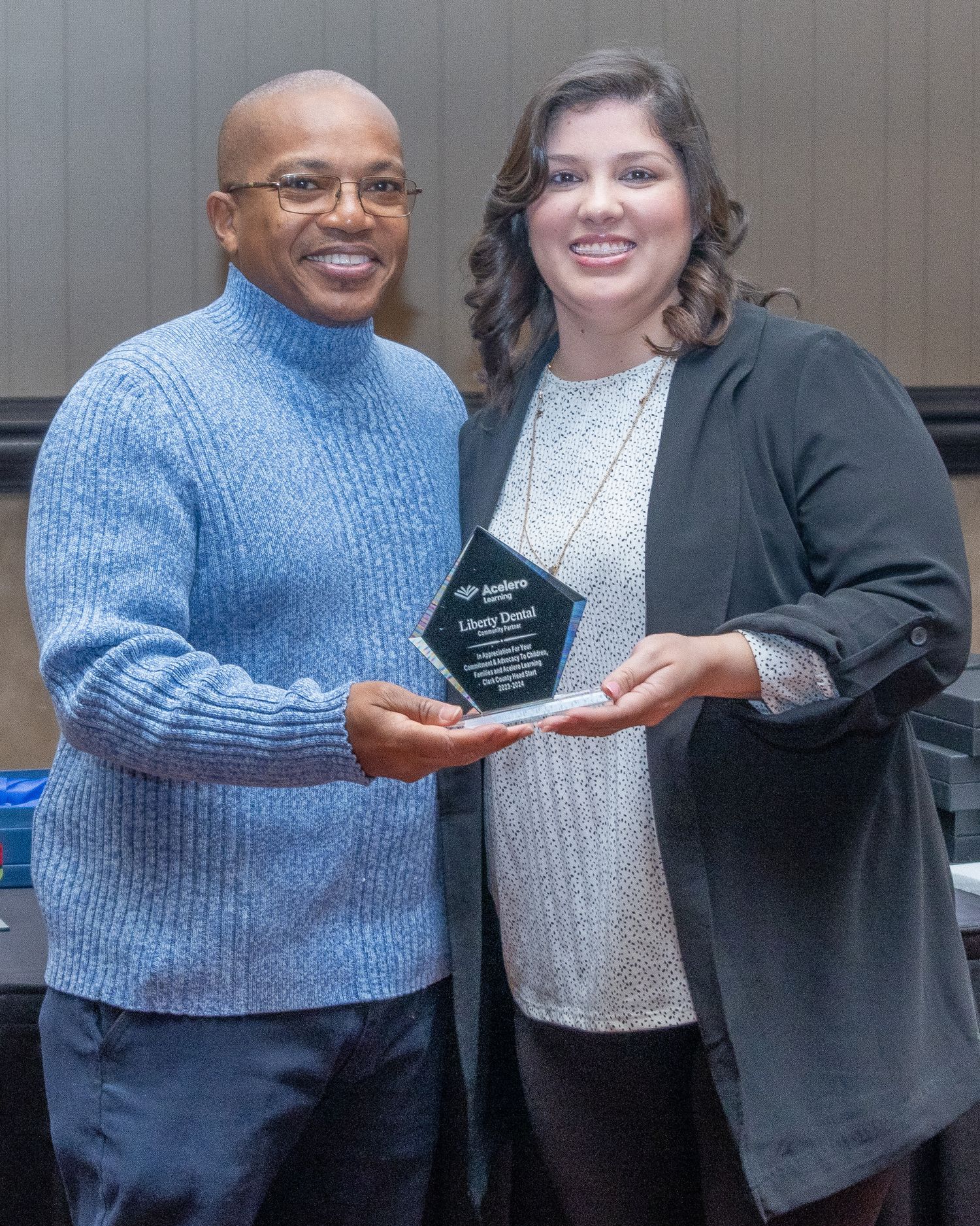 People in business attire pose for photos while exchanging an award plaque at an indoor ceremony.