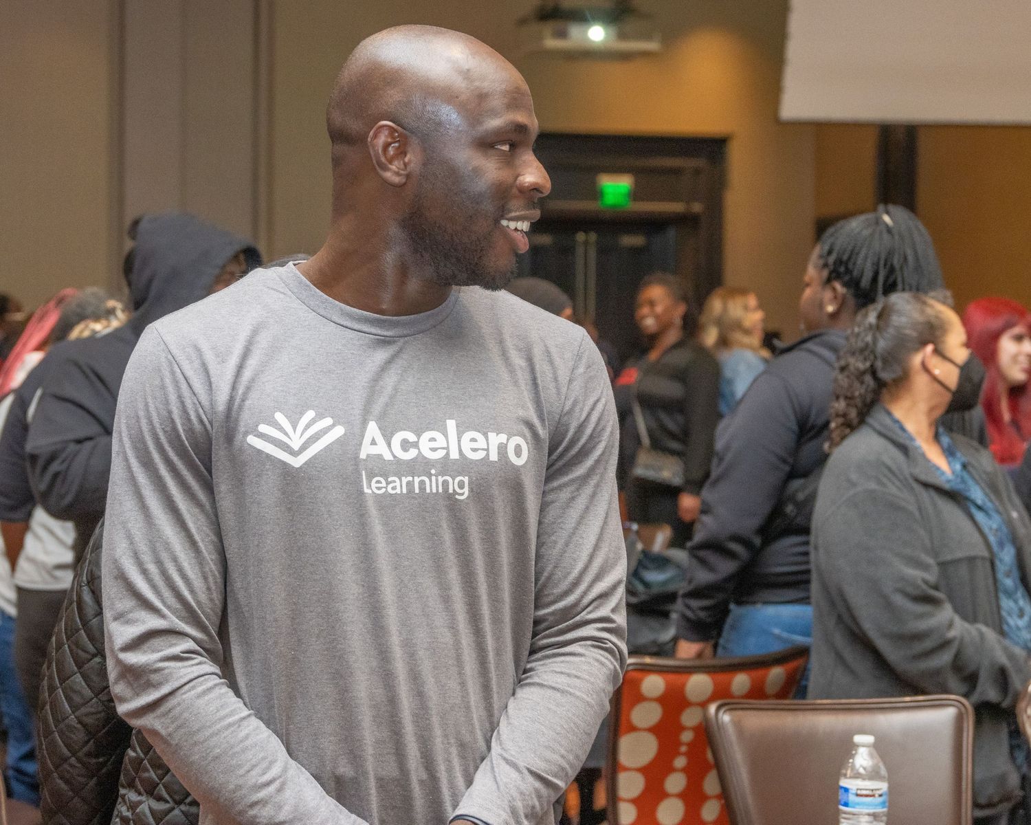 Staff member in gray Acelero shirt smiling during indoor event.