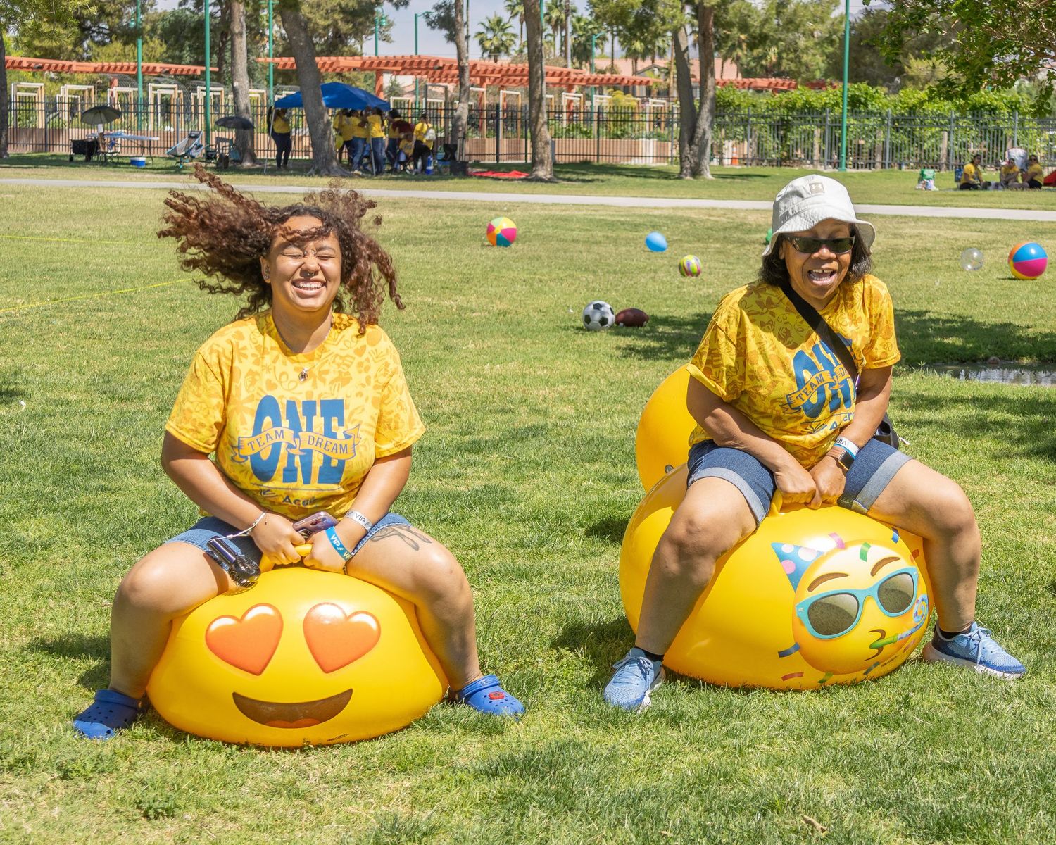 Row of participants sitting on emoji-themed inflatable seats on grass during an outdoor activity.